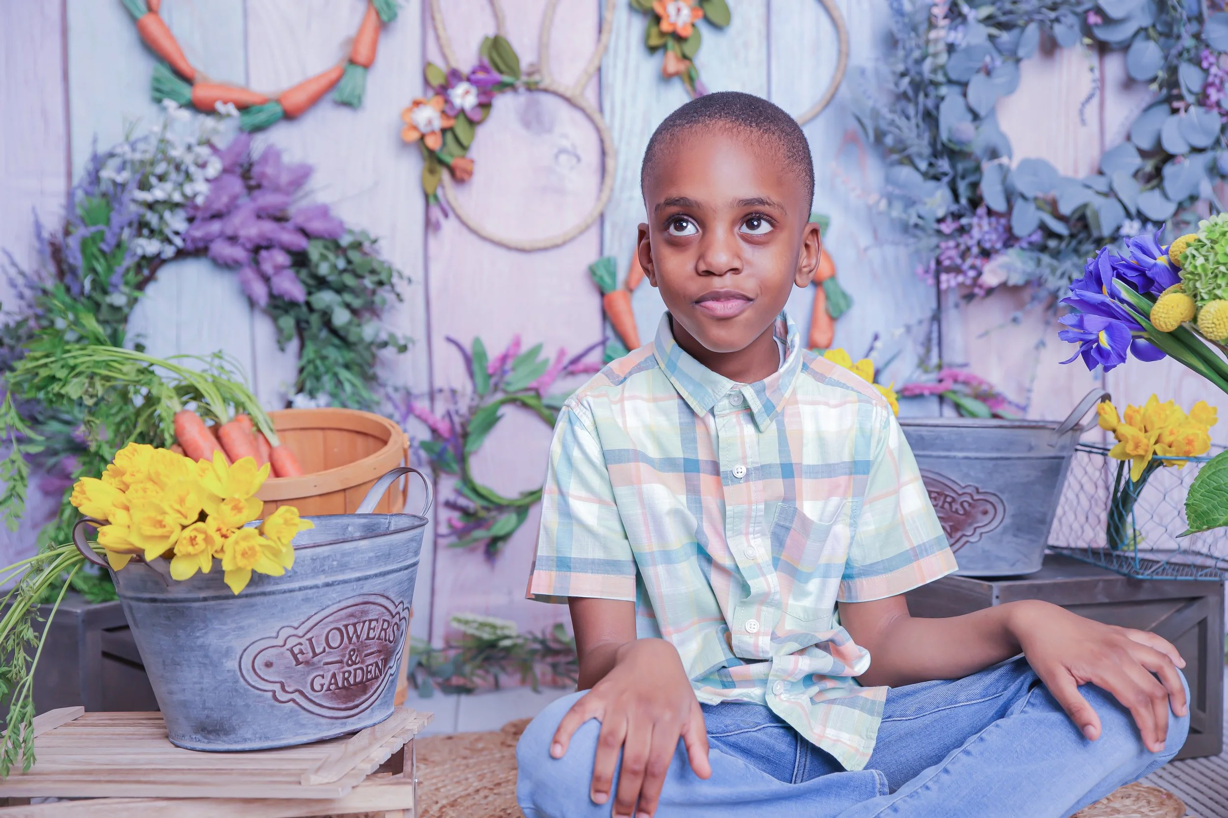 A young boy sitting cross-legged in a flower shop surrounded by colorful flowers and garden decorations.