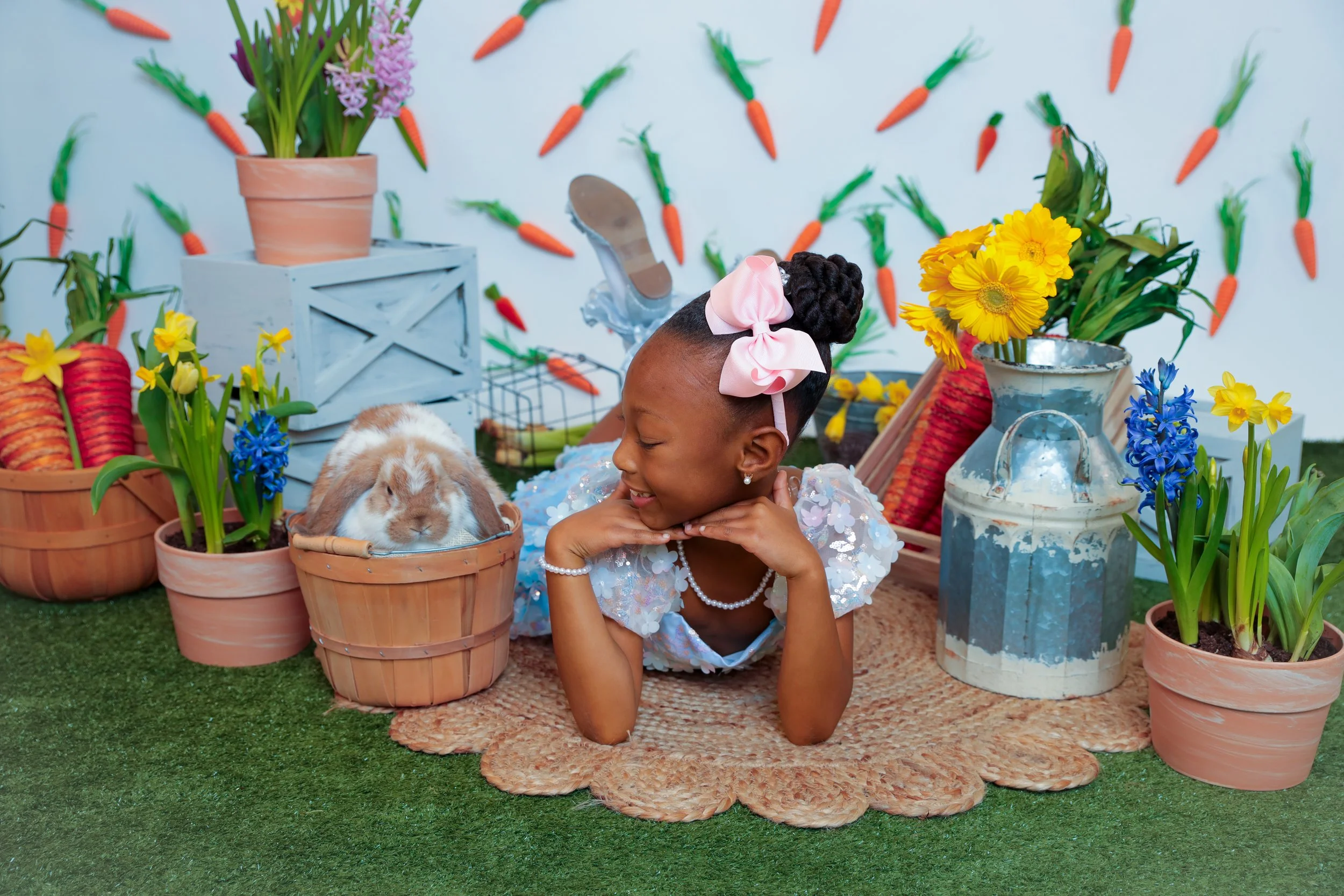 A young girl lying on a rug surrounded by potted flowers and bunny rabbits in a colorful garden setting.