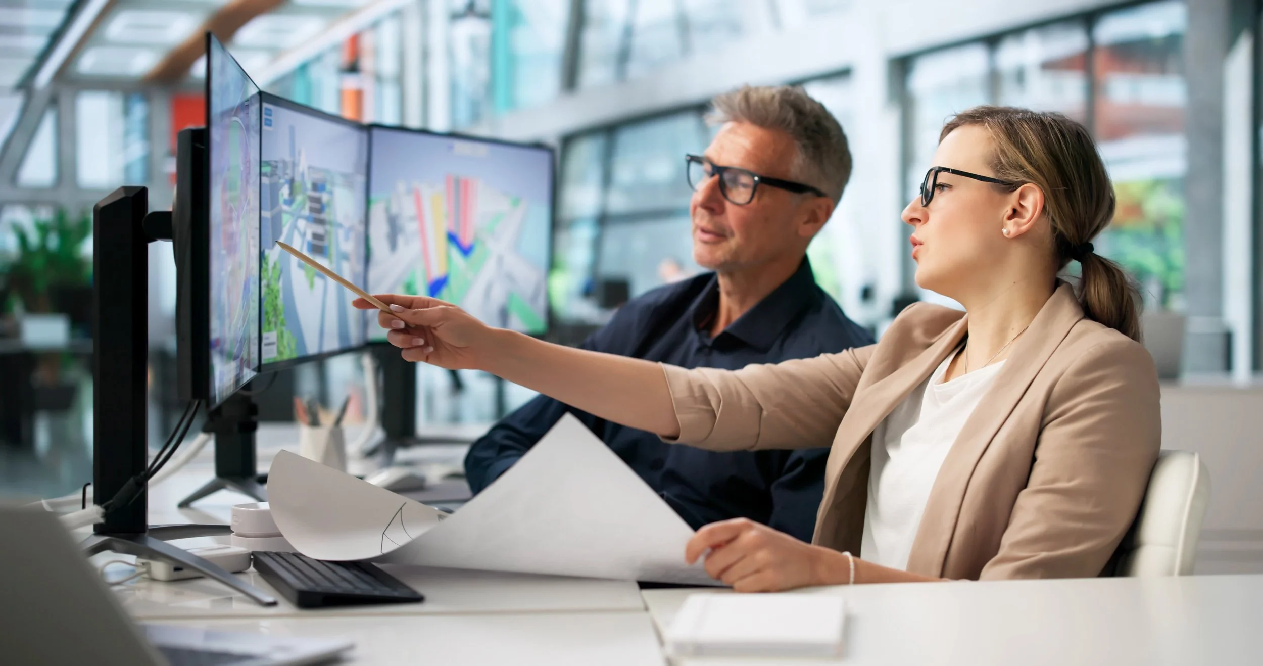 Architects collaborating in a modern studio, reviewing 3D building designs on dual monitors