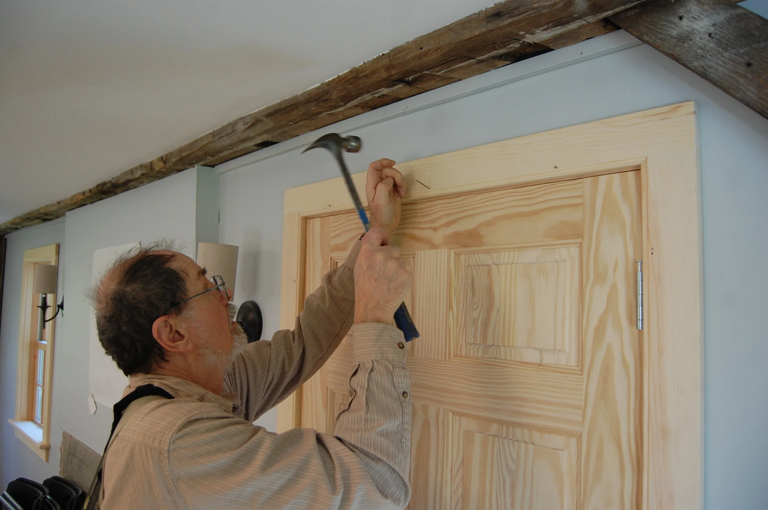 Man hammering a nail into the wall above a wooden door