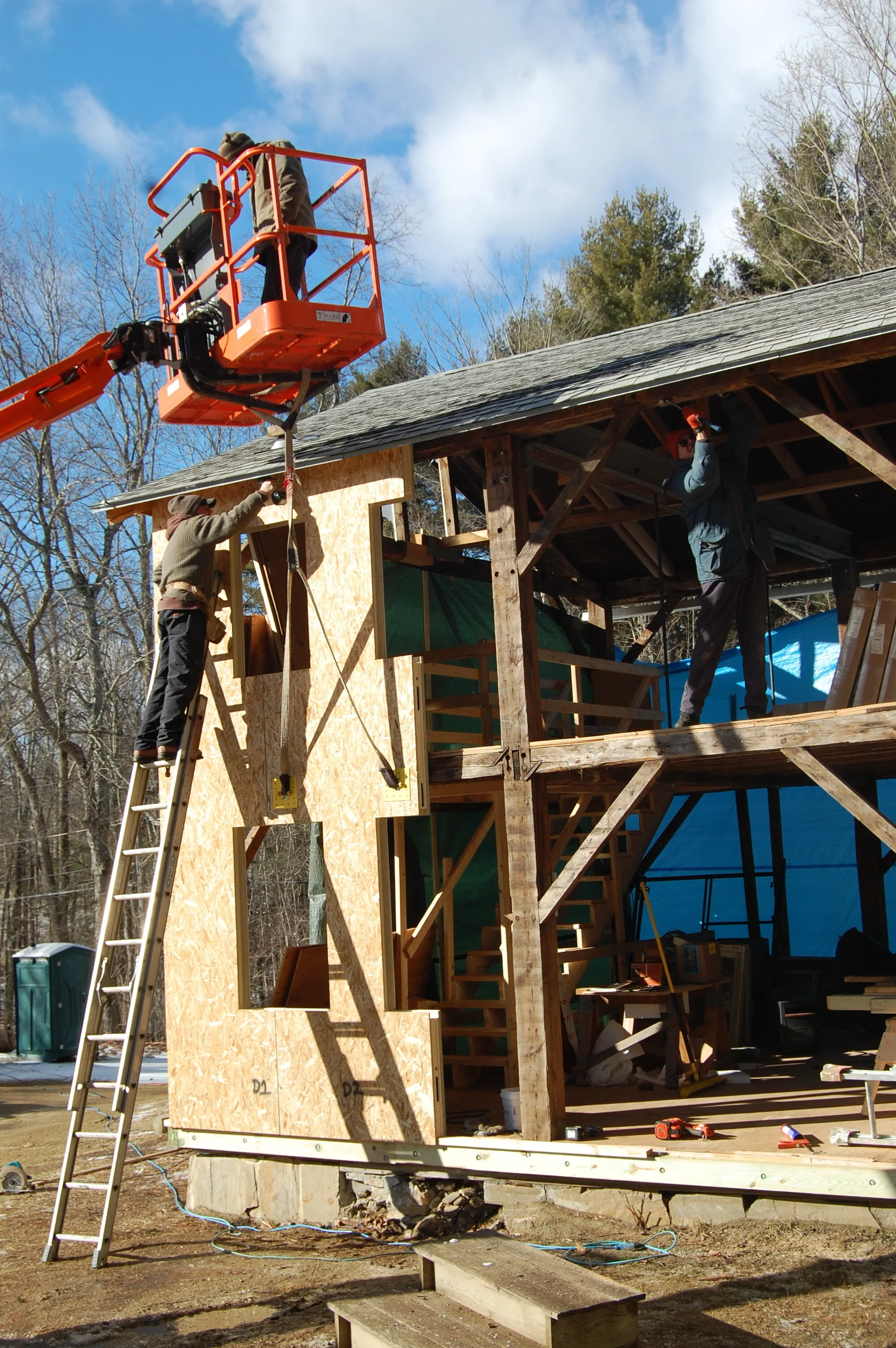 Construction workers building a wooden structure, one on a lift and another on a ladder.