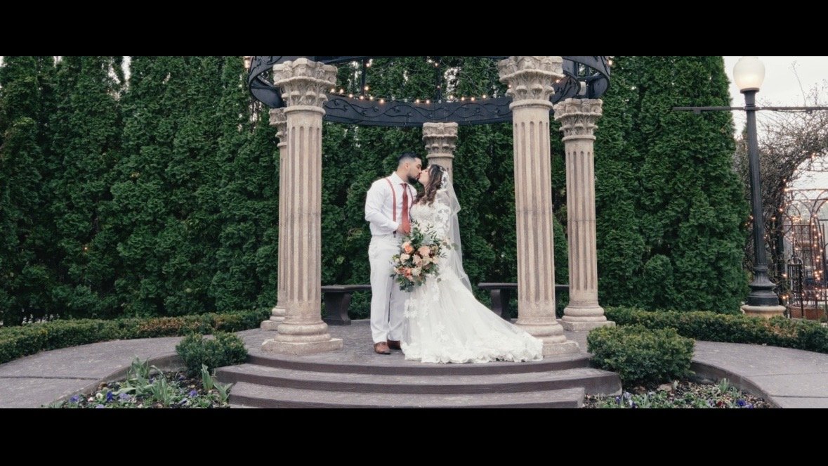 A bride and groom at their venue Le Jardin in Sandy, Utah, standing in a gazebo surrounded by trees.