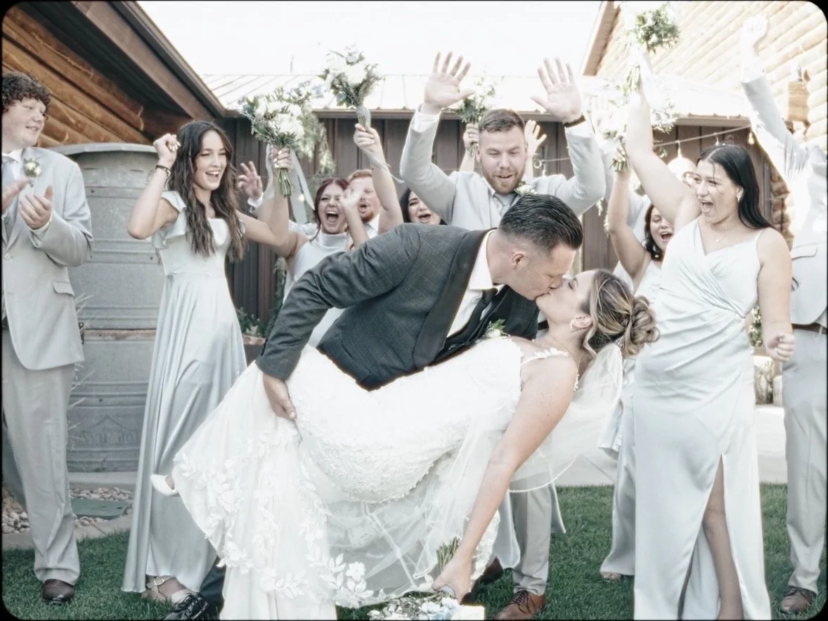 Bridal party cheer as the bride and groom dip and kiss at Cinder Creek Event Center in Nephi, Utah.