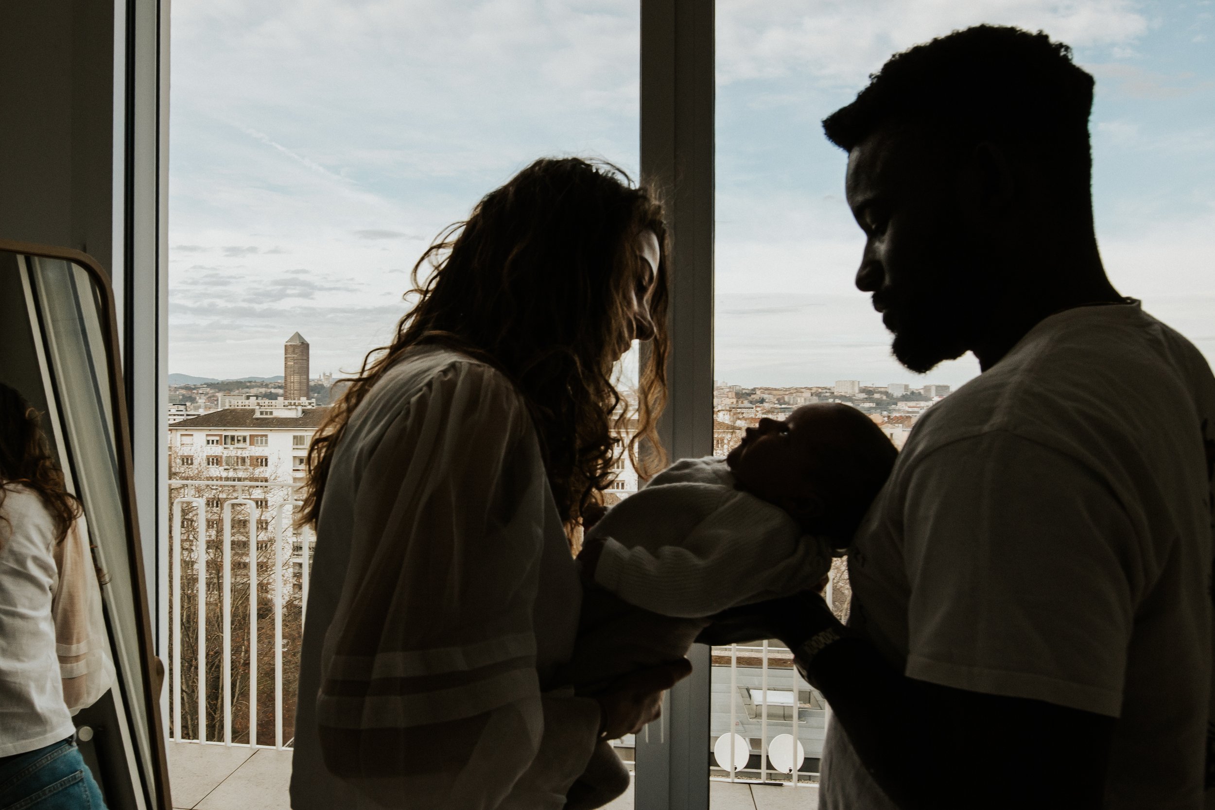 photo d'un couple avec leur nouveau né dans la vue sur les toits de Lyon de leur appartement