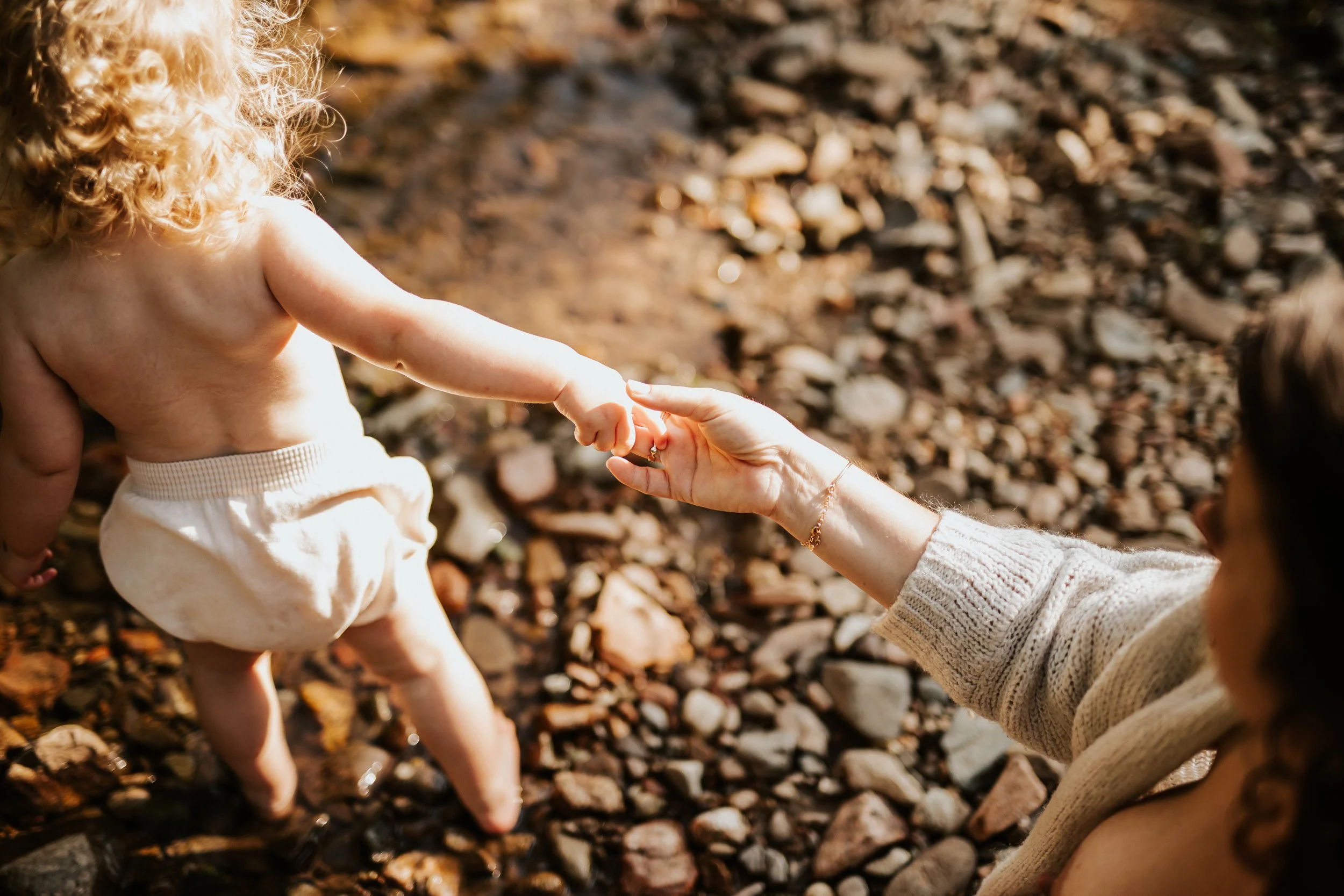 photo de détail d'un bébé pieds nus donnant la main à sa maman entrant dans la rivière dans le beaujolais