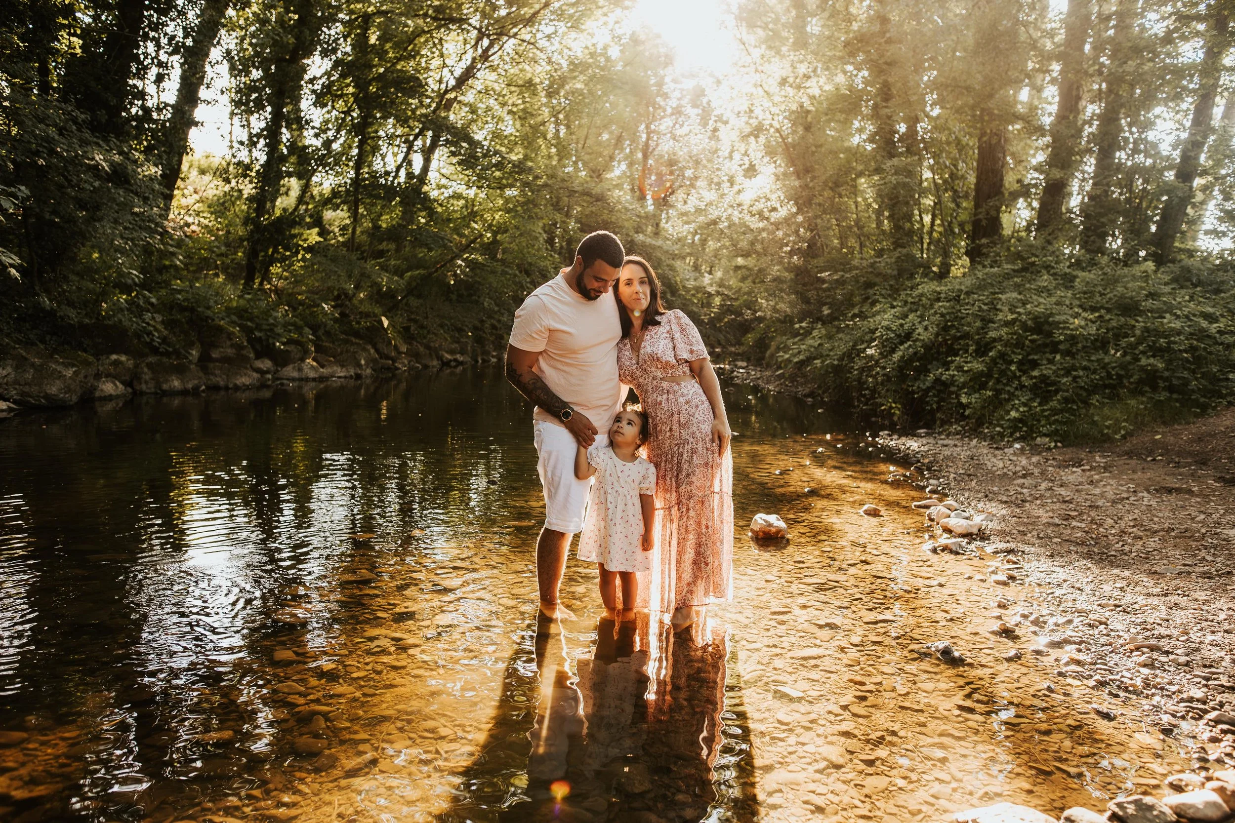 photo d'une magnifique famille les pieds dans une rivière, dans un rayon de soleil à travers les arbres