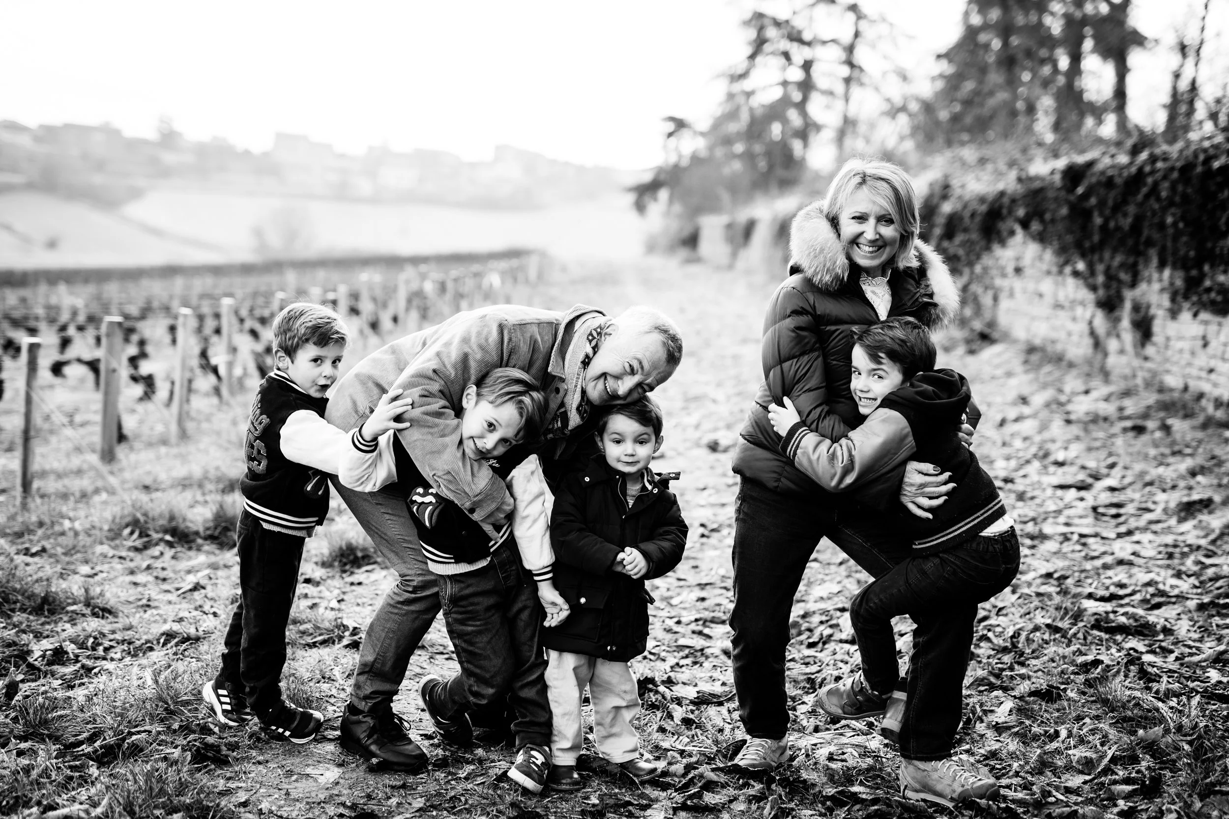 photo en noir et blanc de grand parents avec leurs petits enfants dans un moment de jeu pendant leur séances photos d'hiver dans les vignes