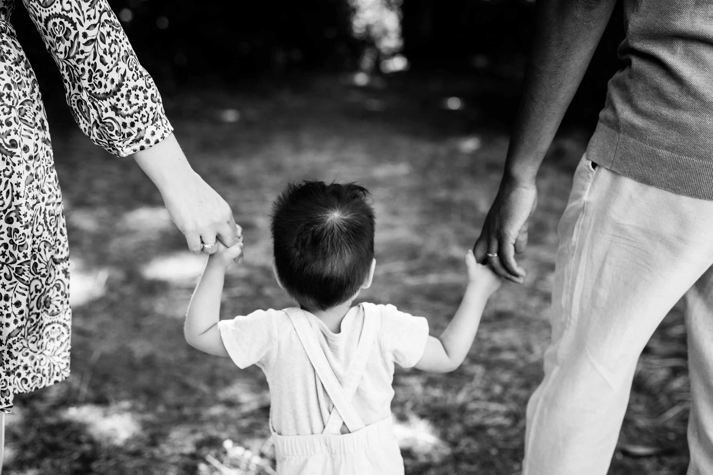 photo noir et blanc d'un bébé de dos main dans la main avec ses parents marchant vers l'eau dans le beaujolais