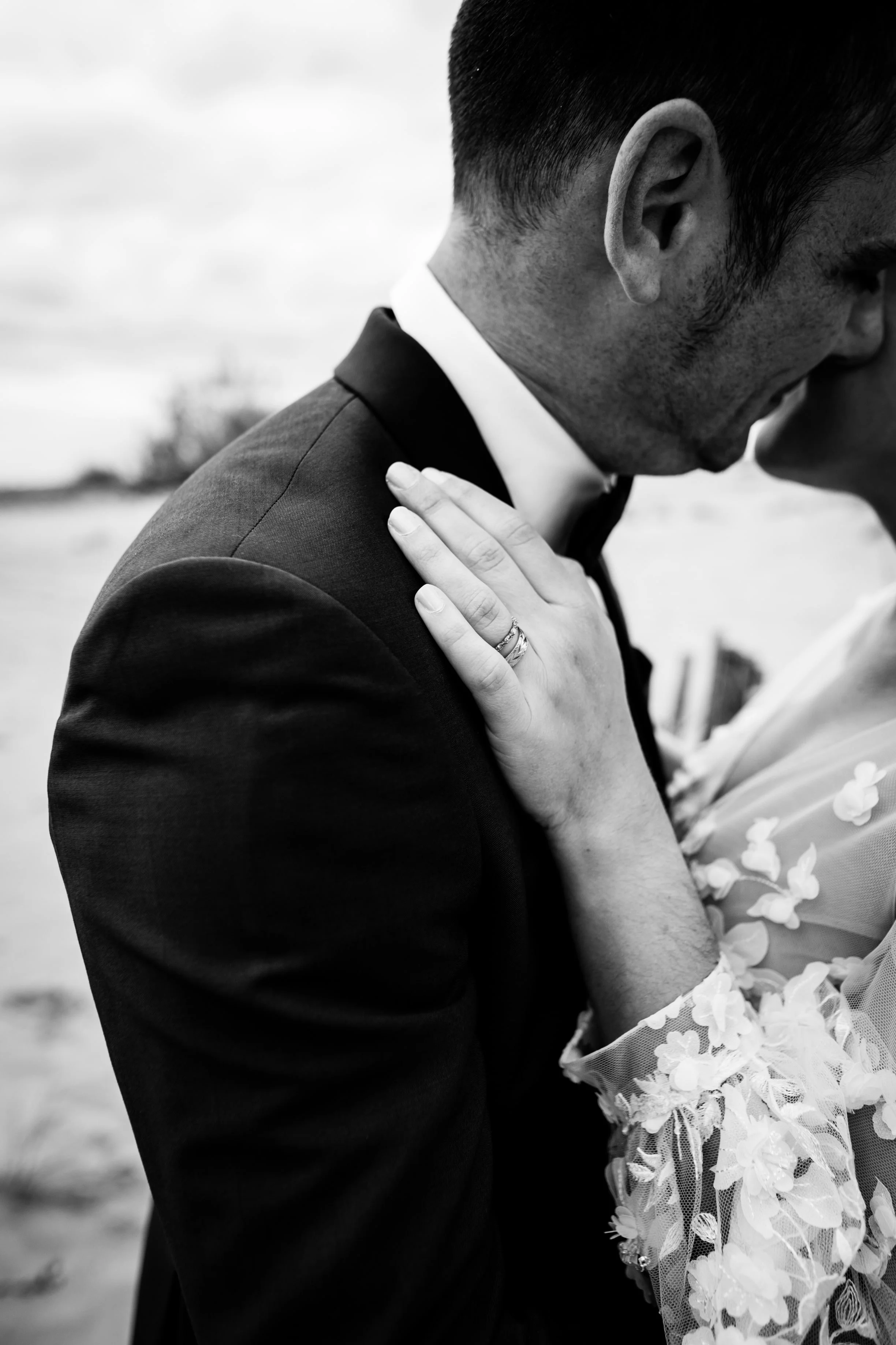 détails en noir et blanc de l'alliance de la mariée et sa bague de fiançaille pendant un calin sur plage