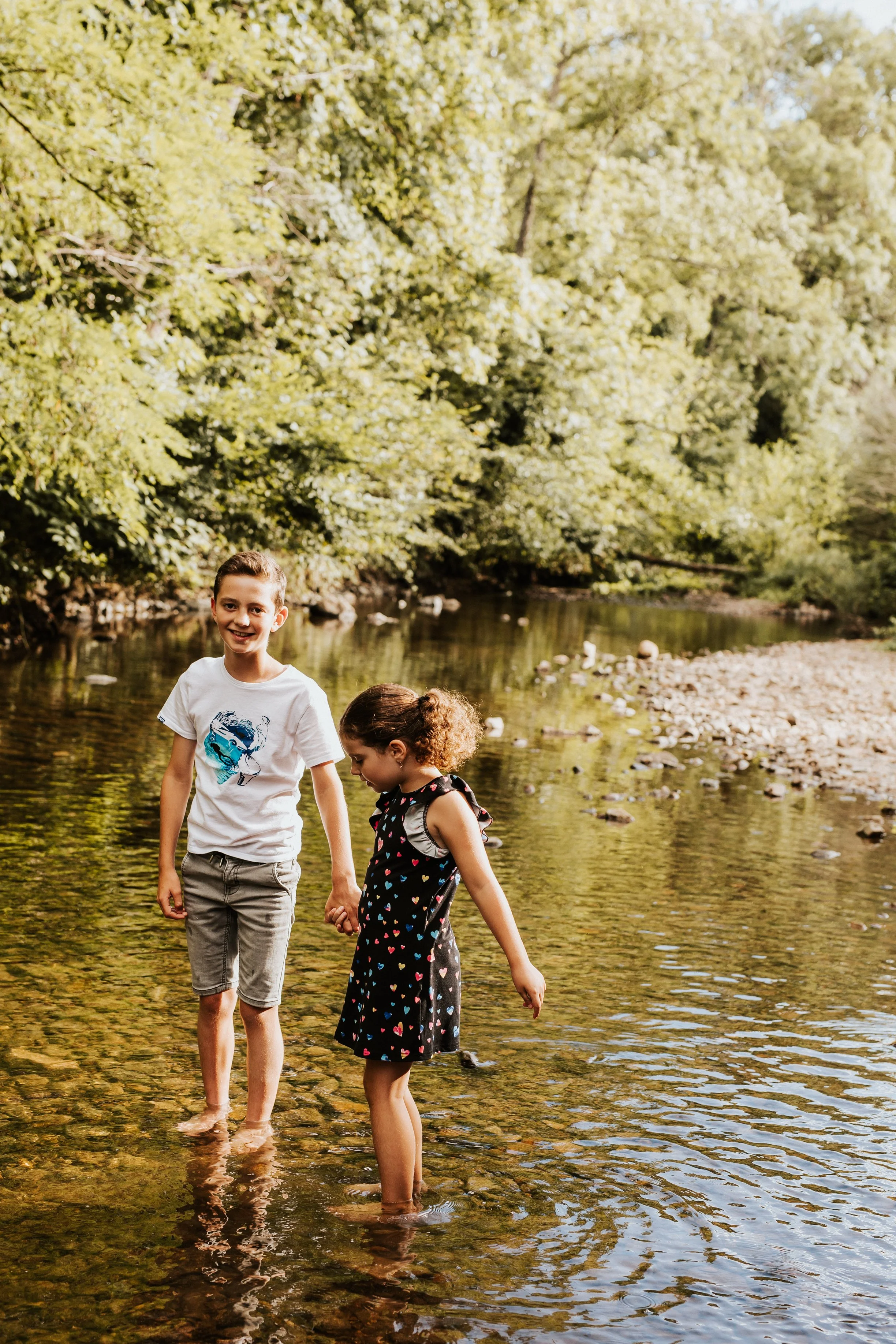 photo de frères et soeur marchant sur les galets dans la rivière pendant leur séance photos en famille dans la nature du beaujolais