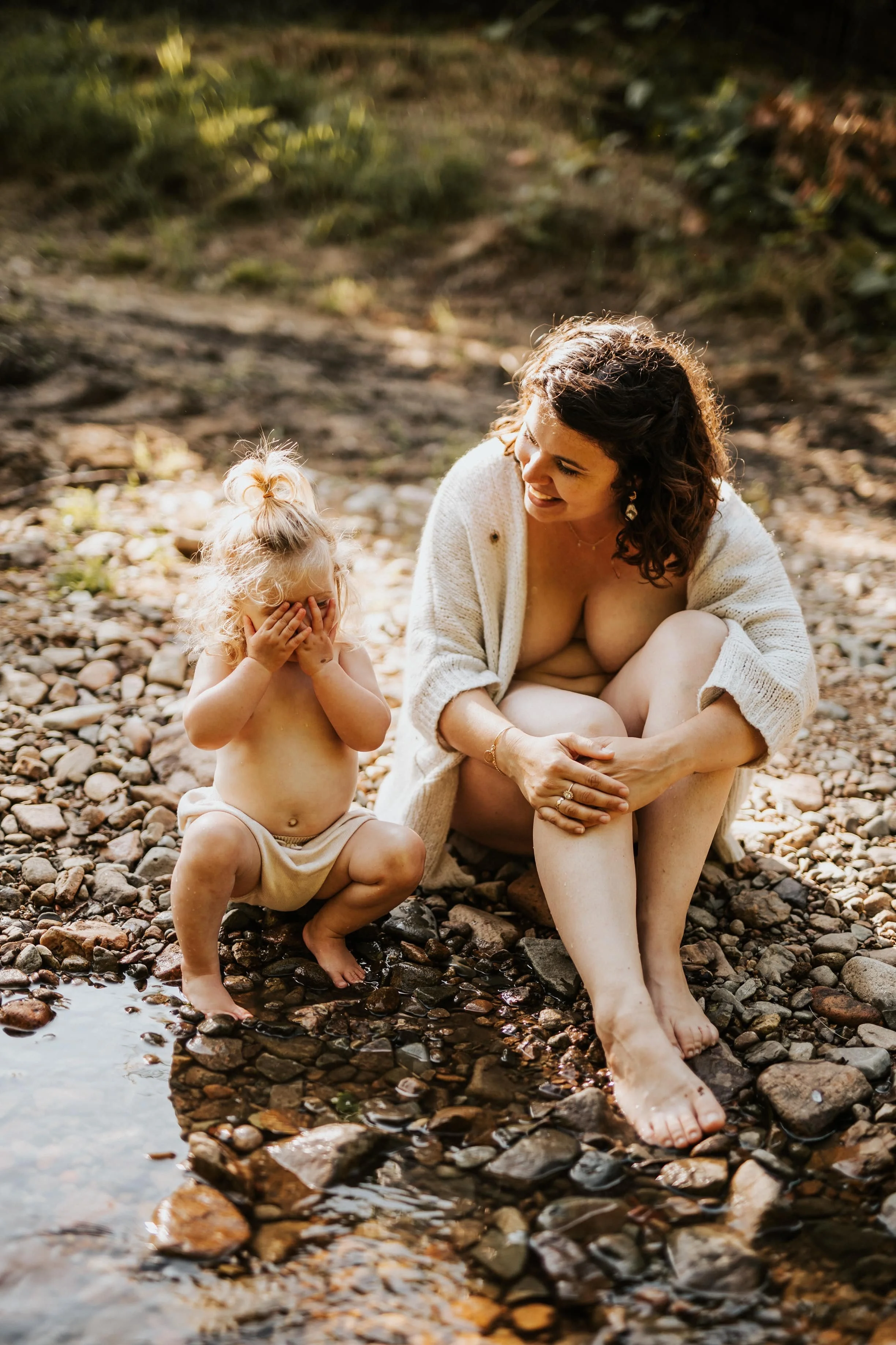 photo d'une maman et sa fille jouant à se cacher derrière ses mains au bord de l'eau dans le beaujolais près de lyon