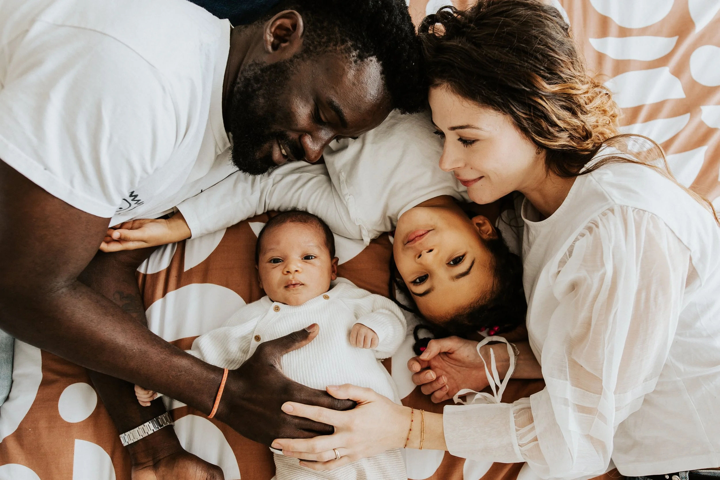 photo d'un moment de tendresse pour une famille aux couleurs de peaux différentes venant d'accueillir un nouveau né pendant leur séance photo à Villeurbanne près de Lyon