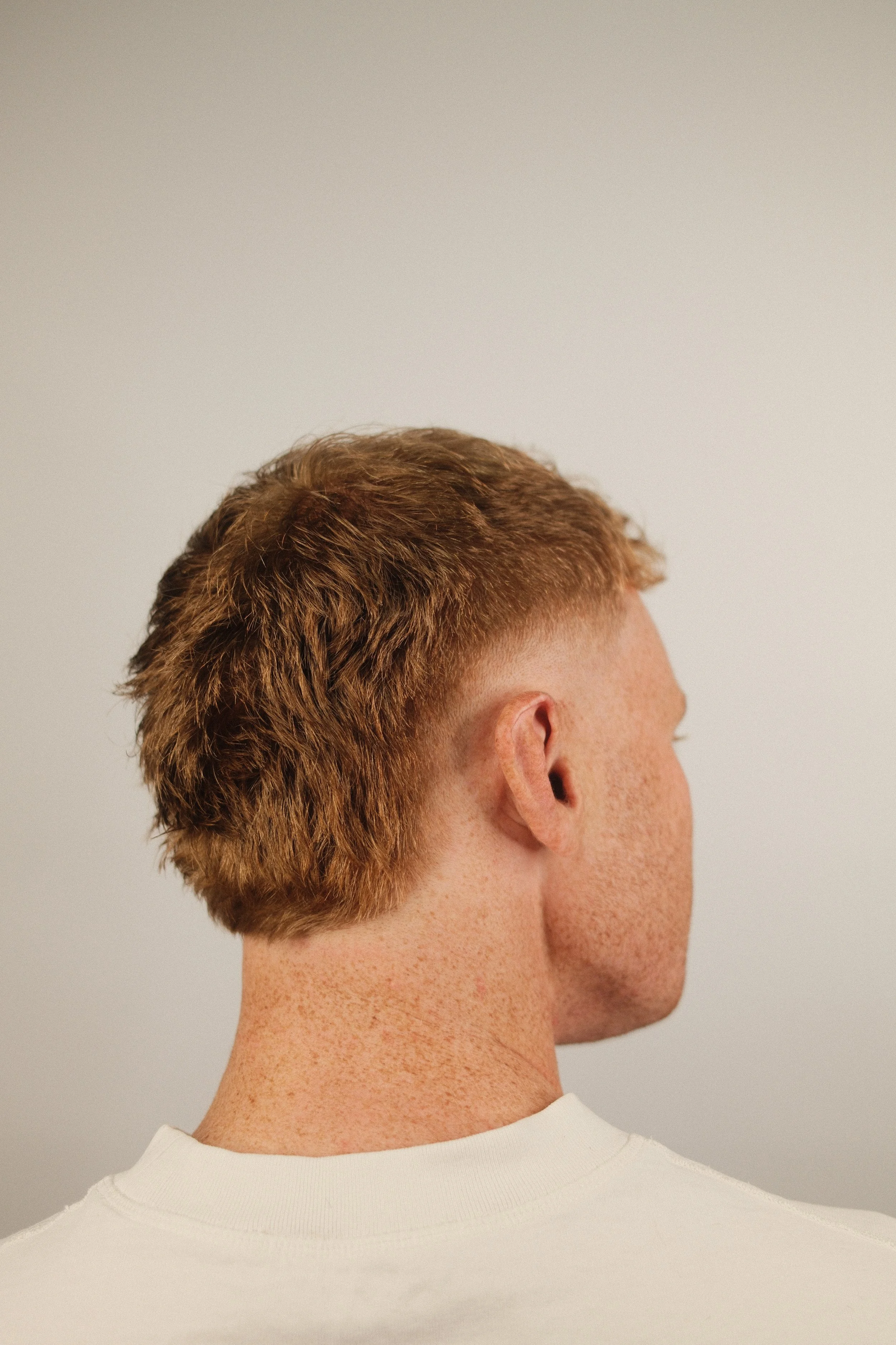 A modern burst fade haircut on a ginger man from the side. the sides are faded short with long flowing back and top.