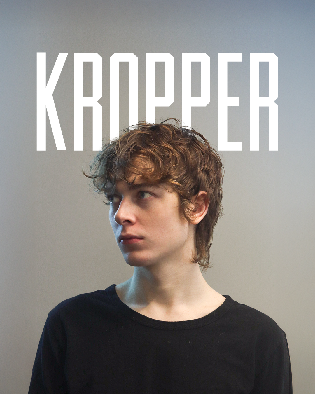 A young person with curly brown hair, wearing a black shirt, looking to the side against a plain gray background with large white text reading 'KRAPPER' above.