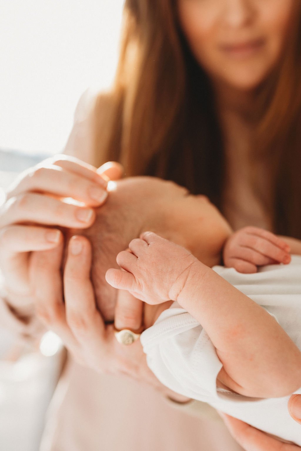 A newborn baby is held in his parents' hands and the camera focuses on the baby's hand which is held up to his head on a newborn photo shoot in Cheltenham