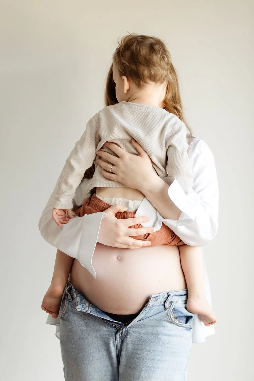 a pregnant mum holds her toddler in front of her so you can see his back and her bump underneath during a maternity photo shoot in Cheltenham.