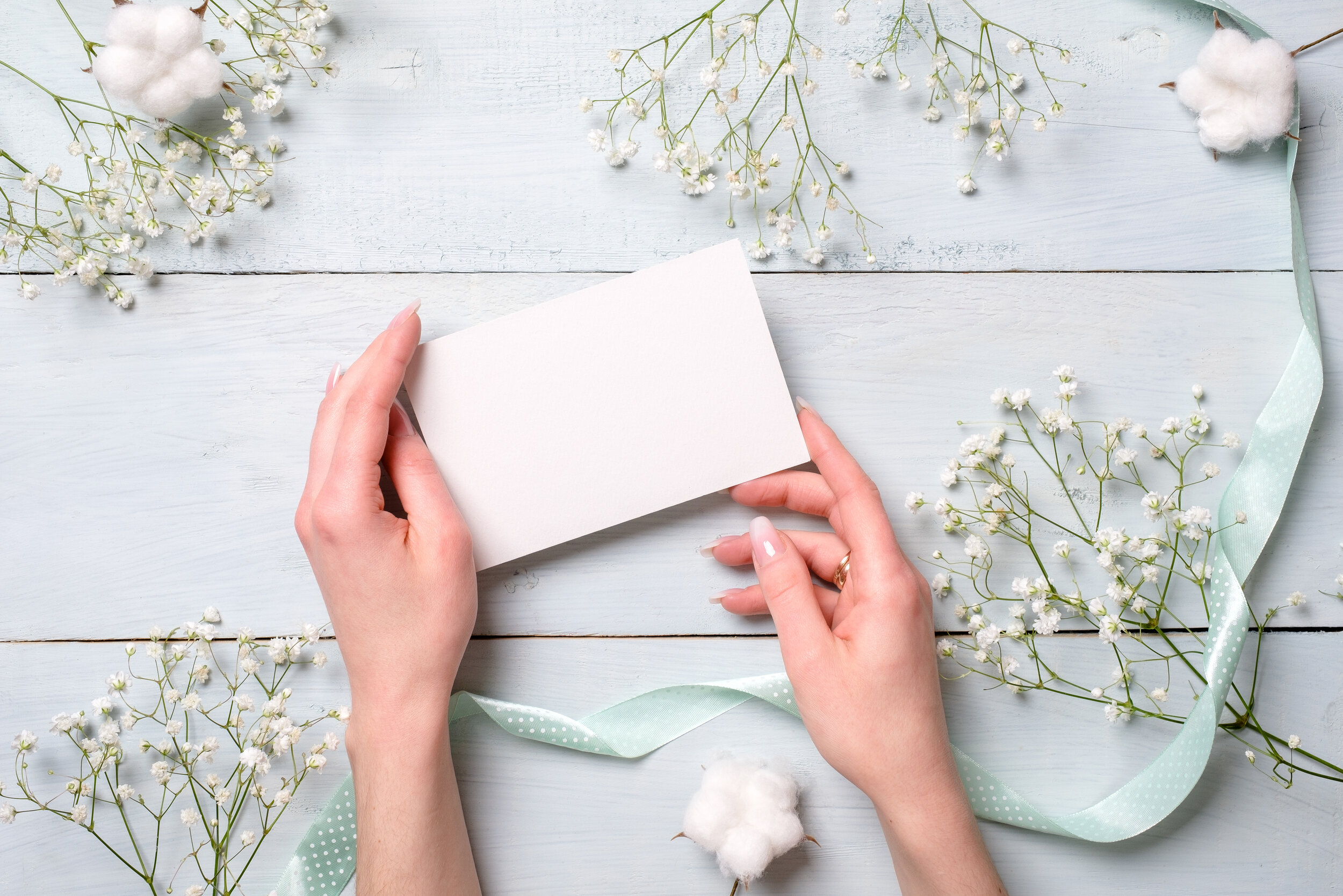 hands-holding-blank-paper-card-light-blue-wooden-desk-with-flowers.jpg