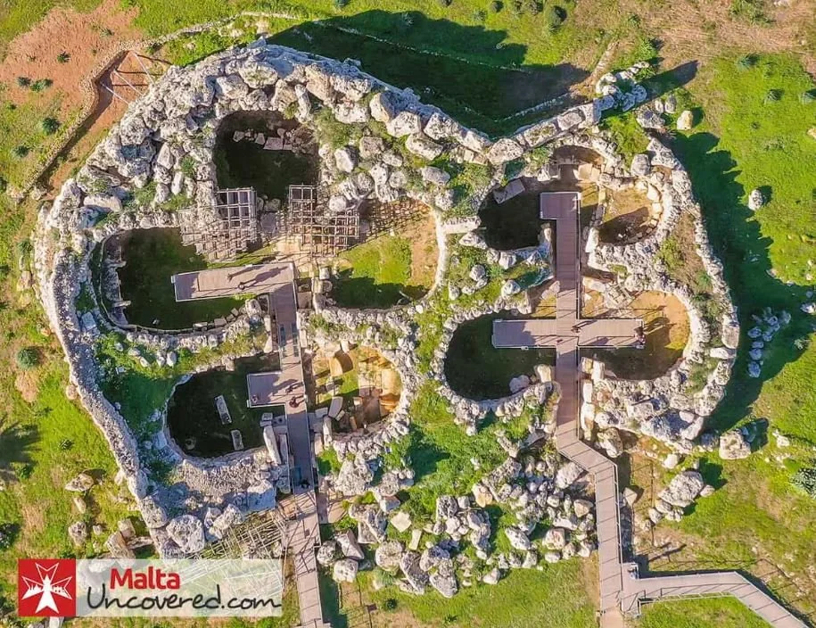 Aerial view of an ancient stone structure in the shape of a large skull, with walkways crossing over the skull's outline and surrounding grassy terrain.
