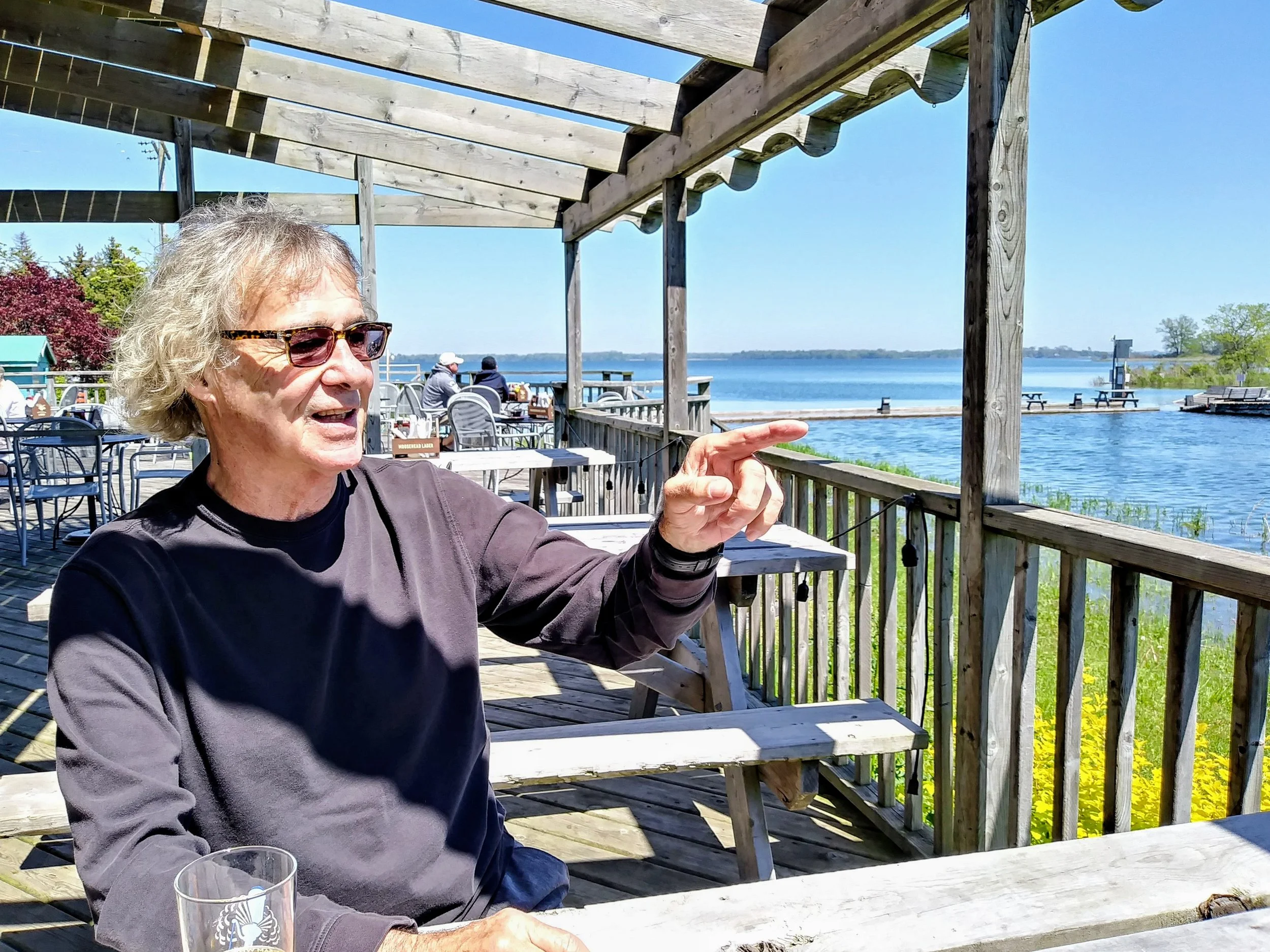 Grant engaged in conversation on the patio of Pounders Pub in Wellington. Sunlight and a clear blue sky await you in Prince Edward County. Ontario's cool climate wine growing region.