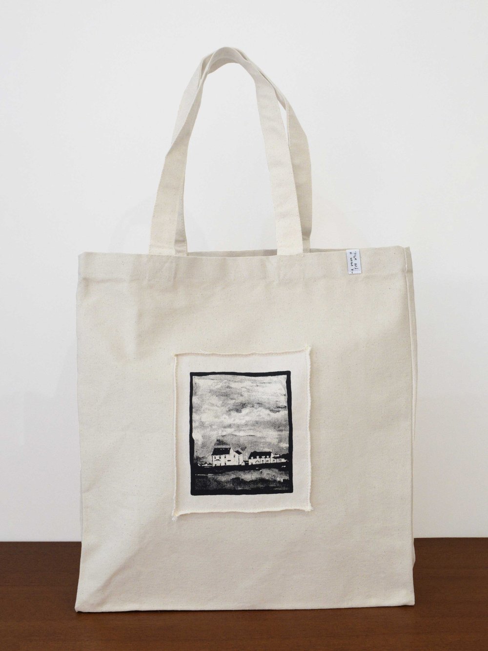 Tote bag by artist, Isobel Hill. Cream tote bag features central silkscreen printed patch of little houses painting in black ink
