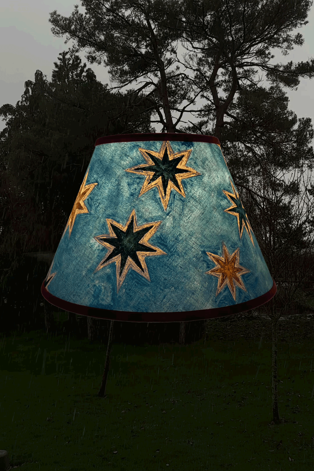 Stars linen lampshade by artist, Isobel Hill. Lamp is rotating whilst glowing, snow falls in the background.