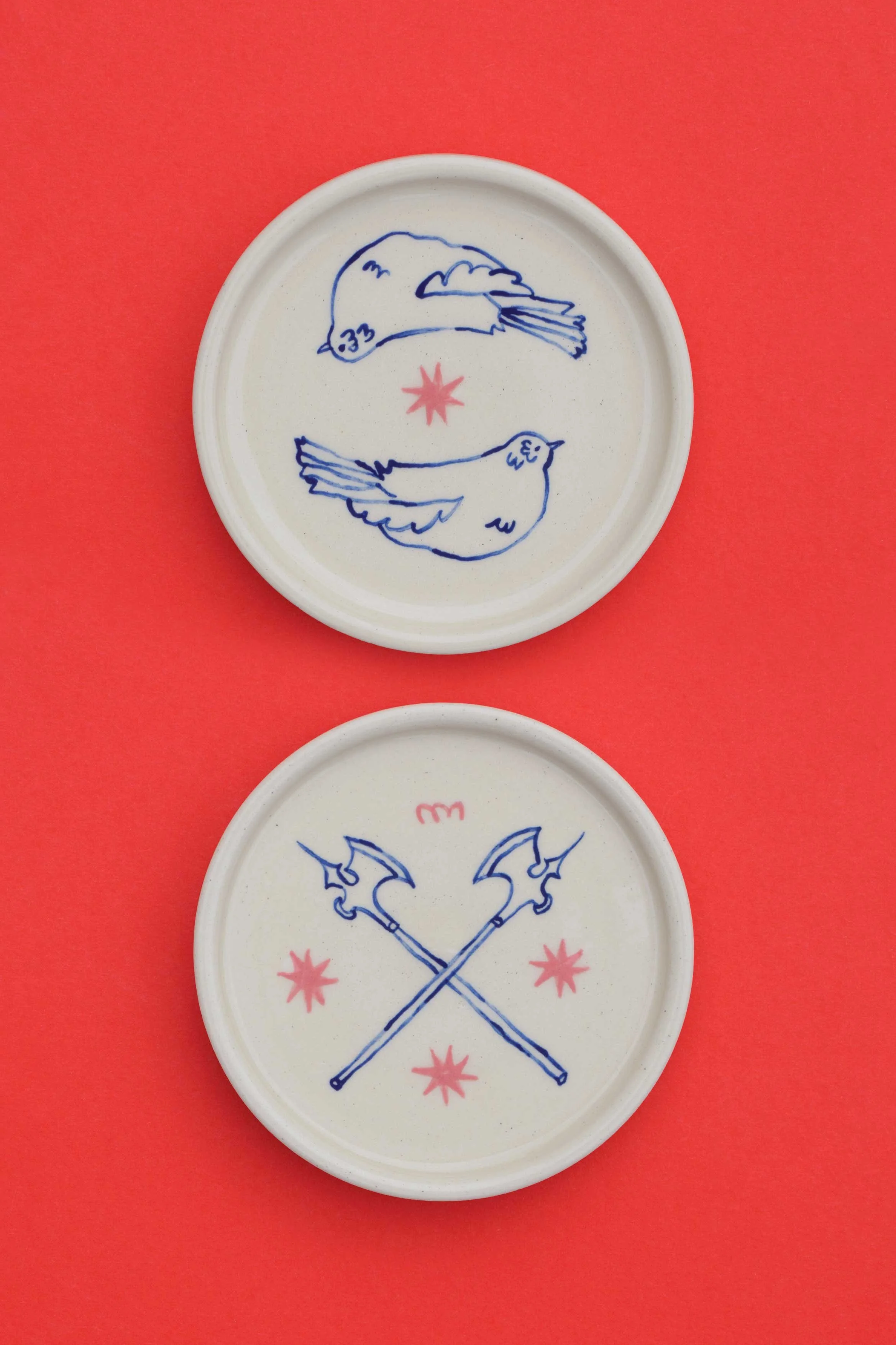 Stoneware ceramic coaster set by artist, Isobel Hill, featuring two mirroring birds, pink stars and blue axes.