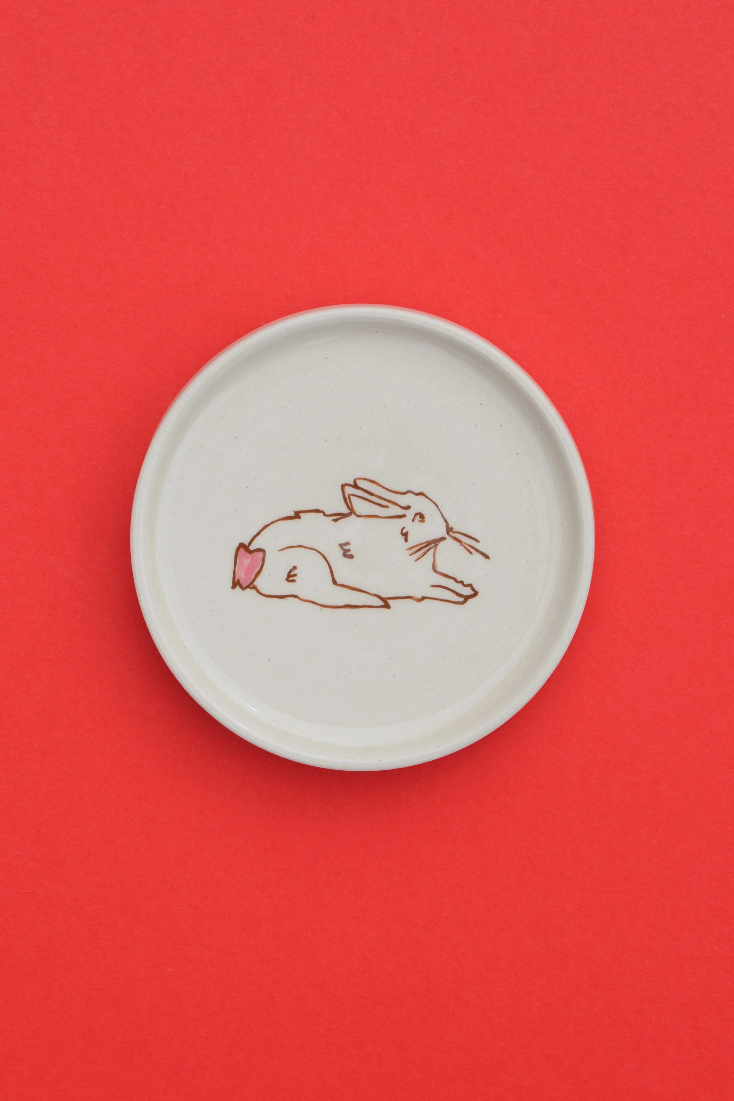 Stoneware ceramic coaster set by artist, Isobel Hill, featuring a brown rabbit laying down. The rabbit has a pink heart tail.