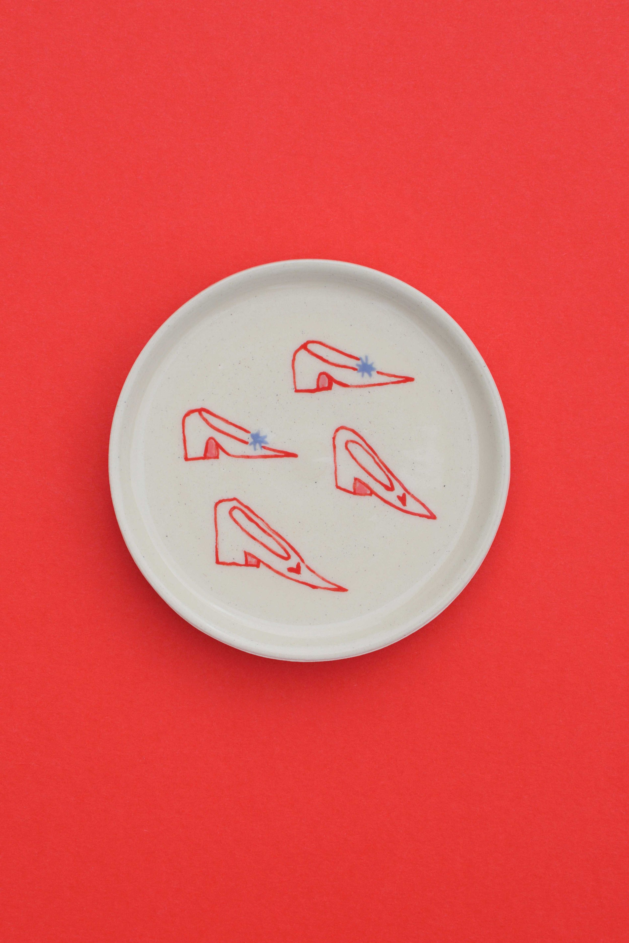 Stoneware ceramic coaster set by artist, Isobel Hill, featuring a collection of red, pink and periwinkle heeled shoes.