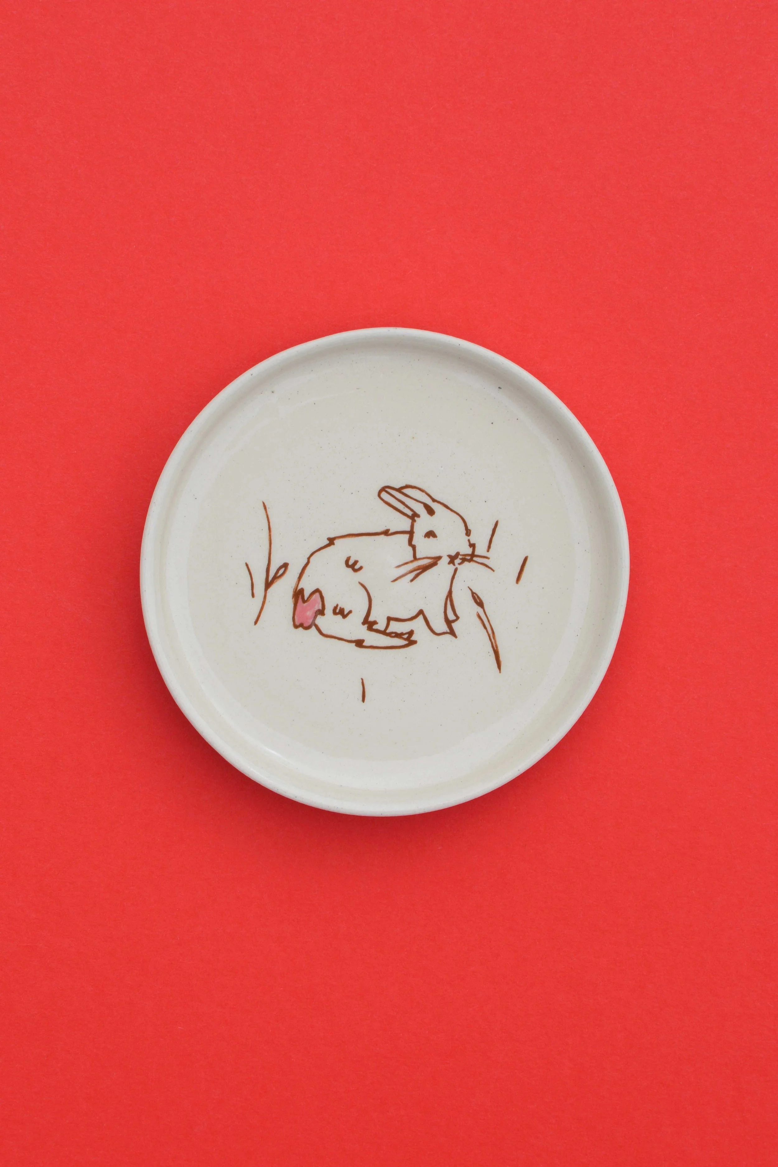 Stoneware ceramic coaster set by artist, Isobel Hill, featuring a brown rabbit with a pink heart tail sitting down.