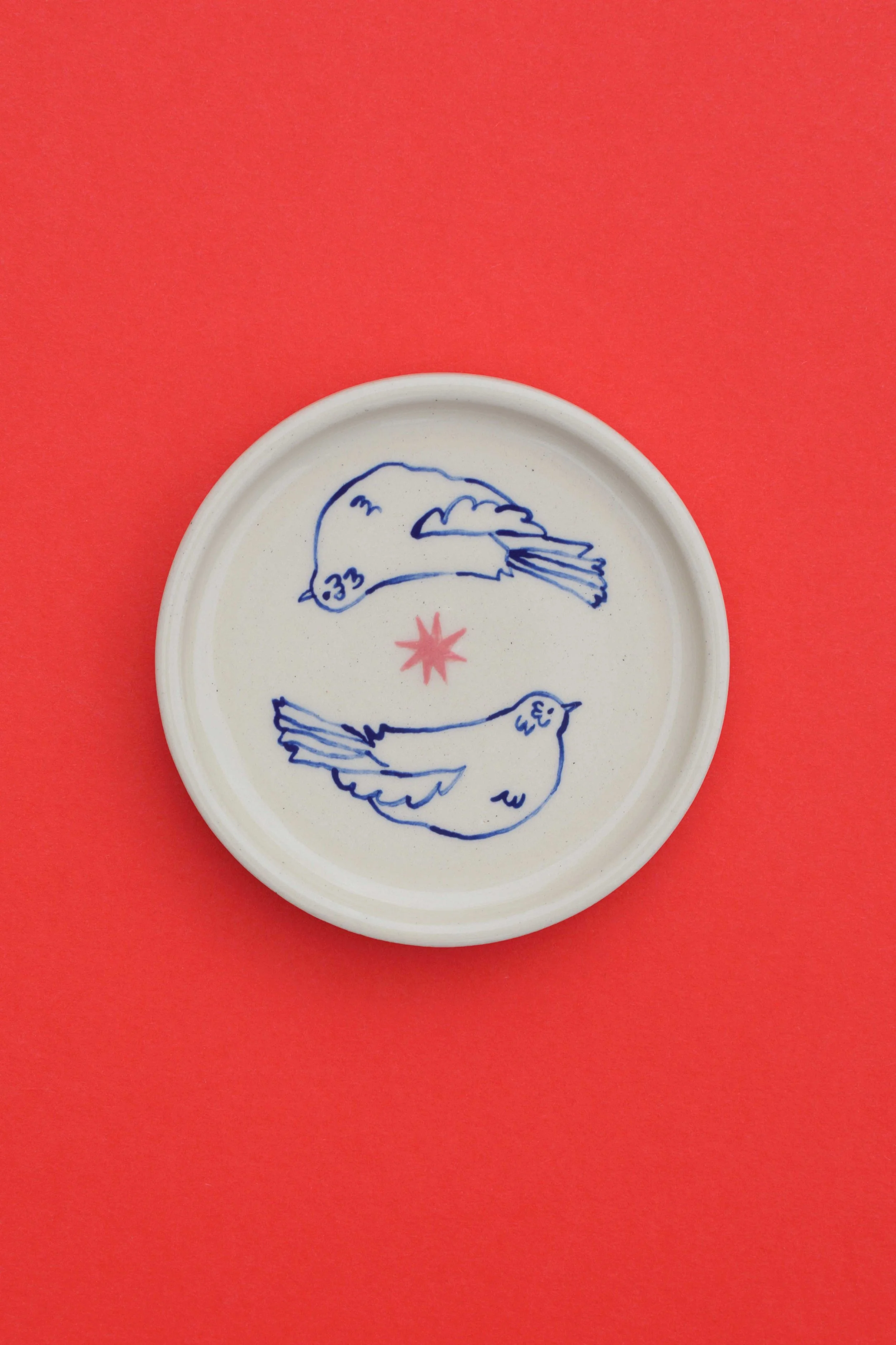 Stoneware ceramic coaster set by artist, Isobel Hill, featuring two circling mirroring birds and a pink star.