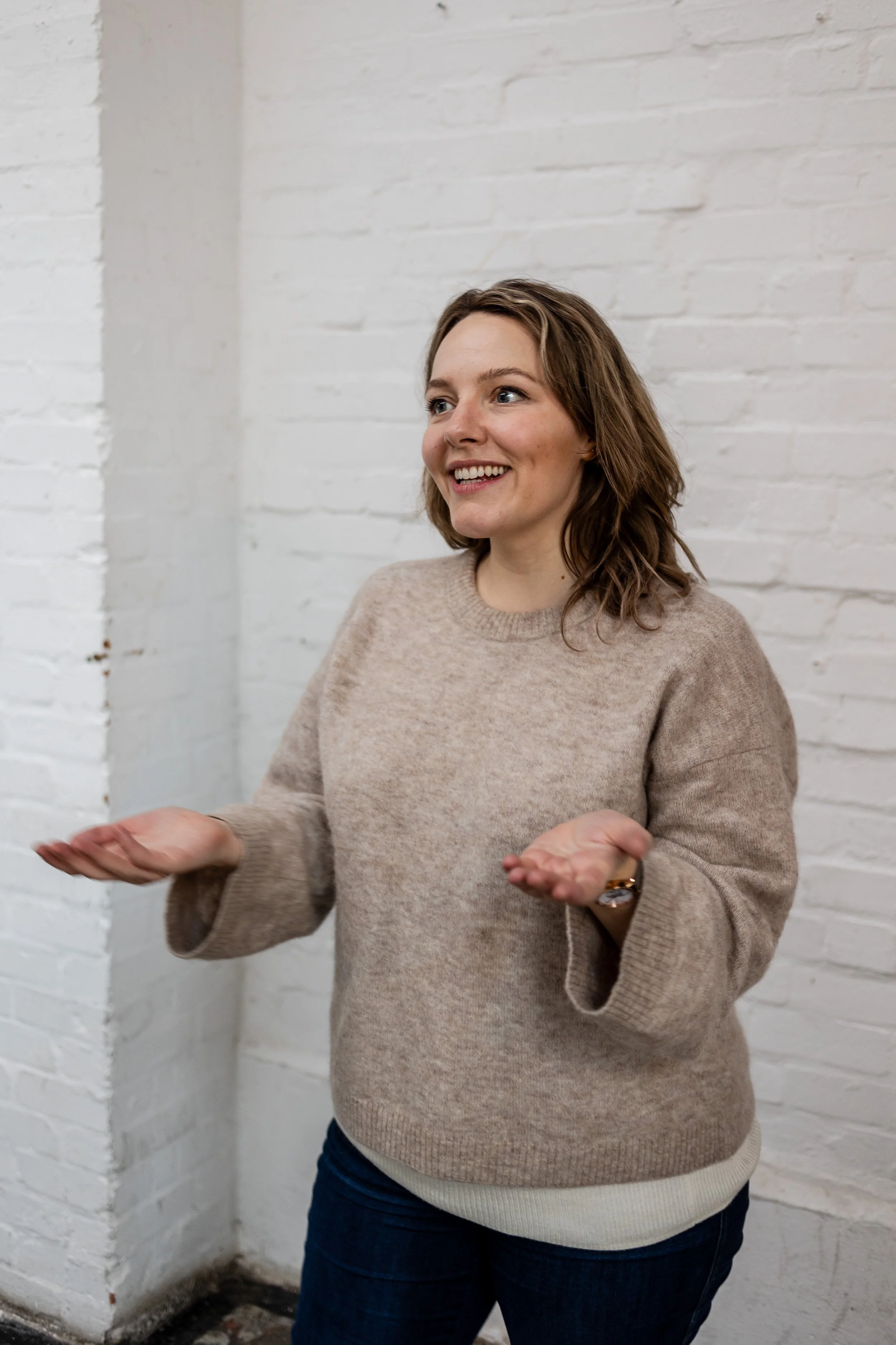 Ettie is a white person with shoulder-length light brown hair. She’s wearing a cosy beige jumper, speaking to an audience off camera. Her hands are open and welcoming with a kind smile on her face.