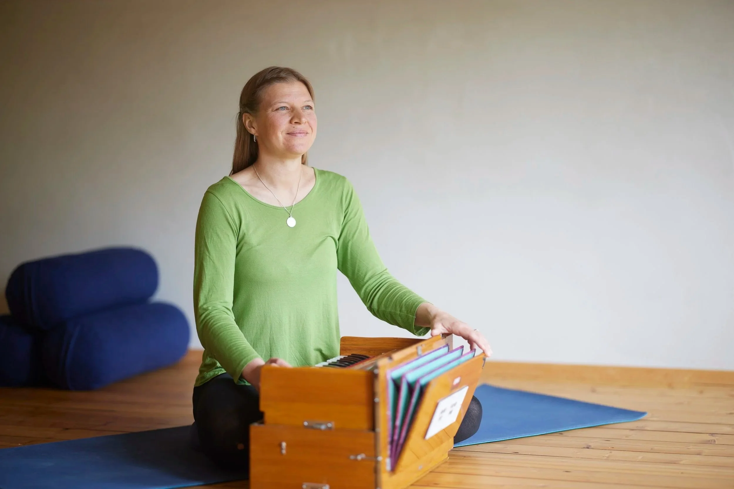 Kvinne sitter med smil og spiller harmonium