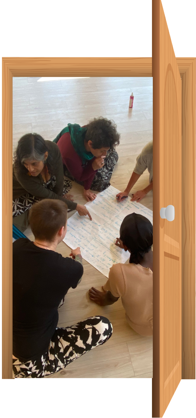 Group of people collaborating around a handwritten poster on the floor, viewed through a wooden doorway