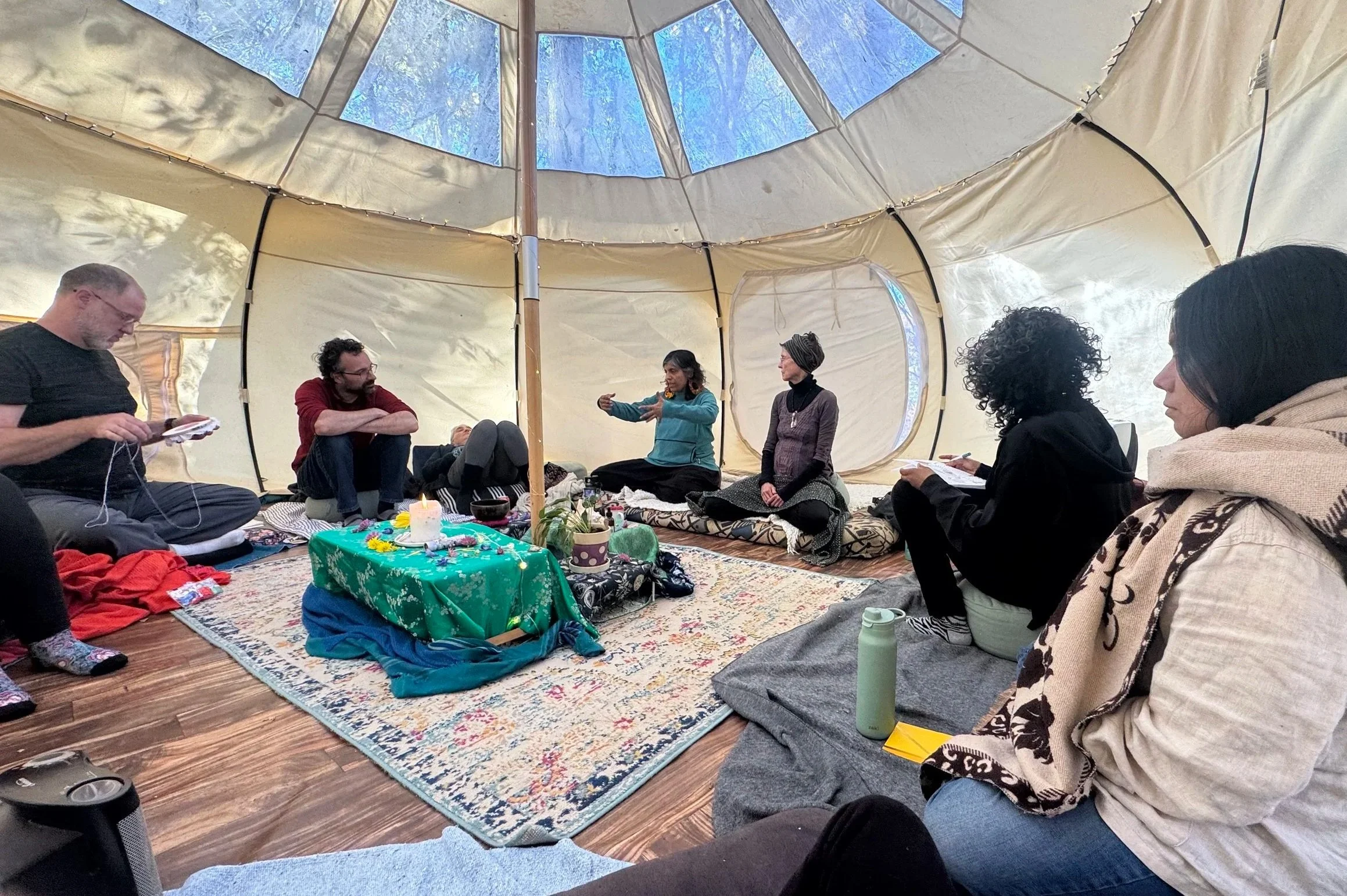 Group of adults sitting in a canvas tent around a decorated table during a discussion or gathering