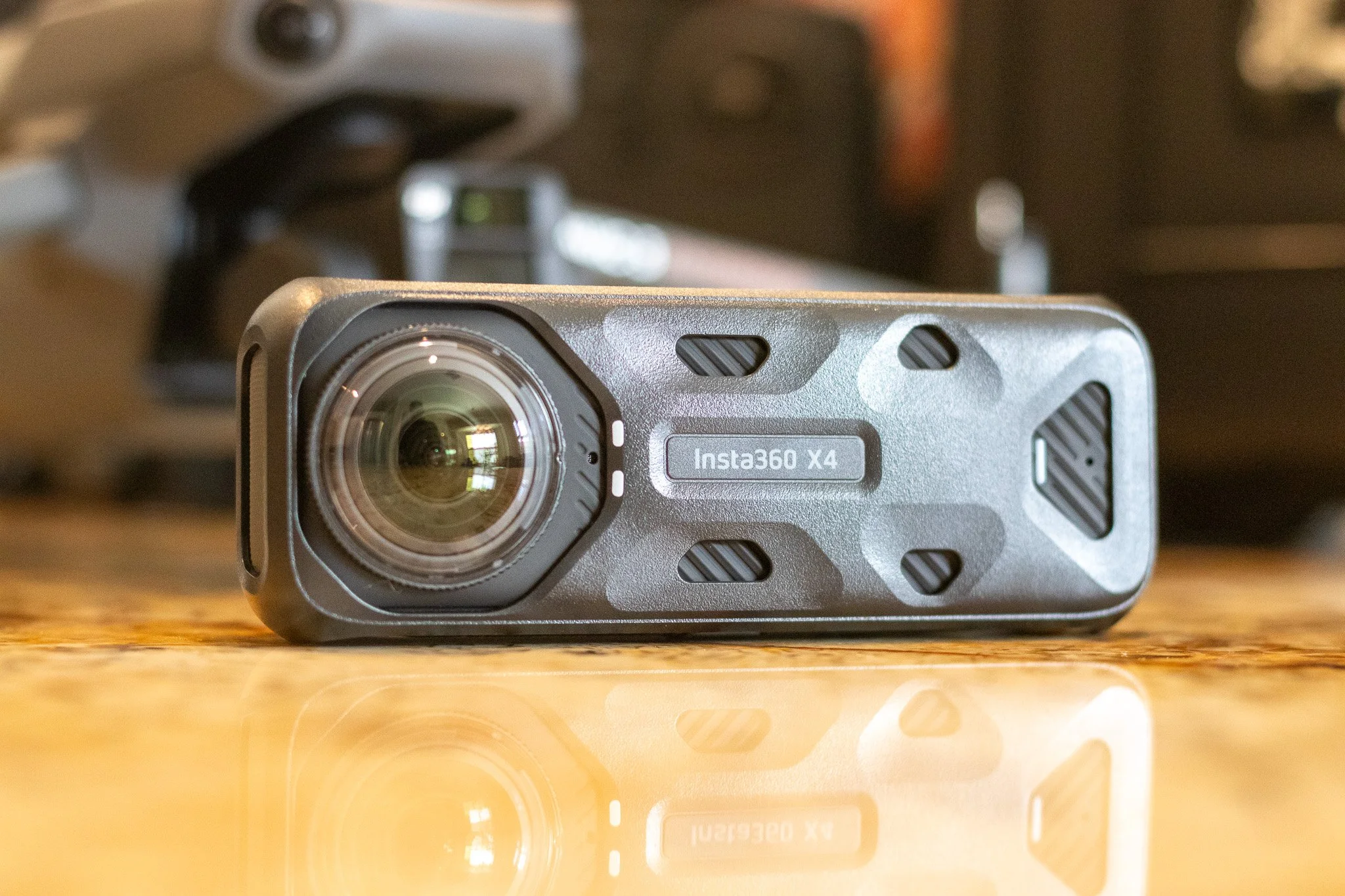 Close-up of a rugged action camera labeled Insta360 X4 on a wooden surface, with blurred equipment in the background.