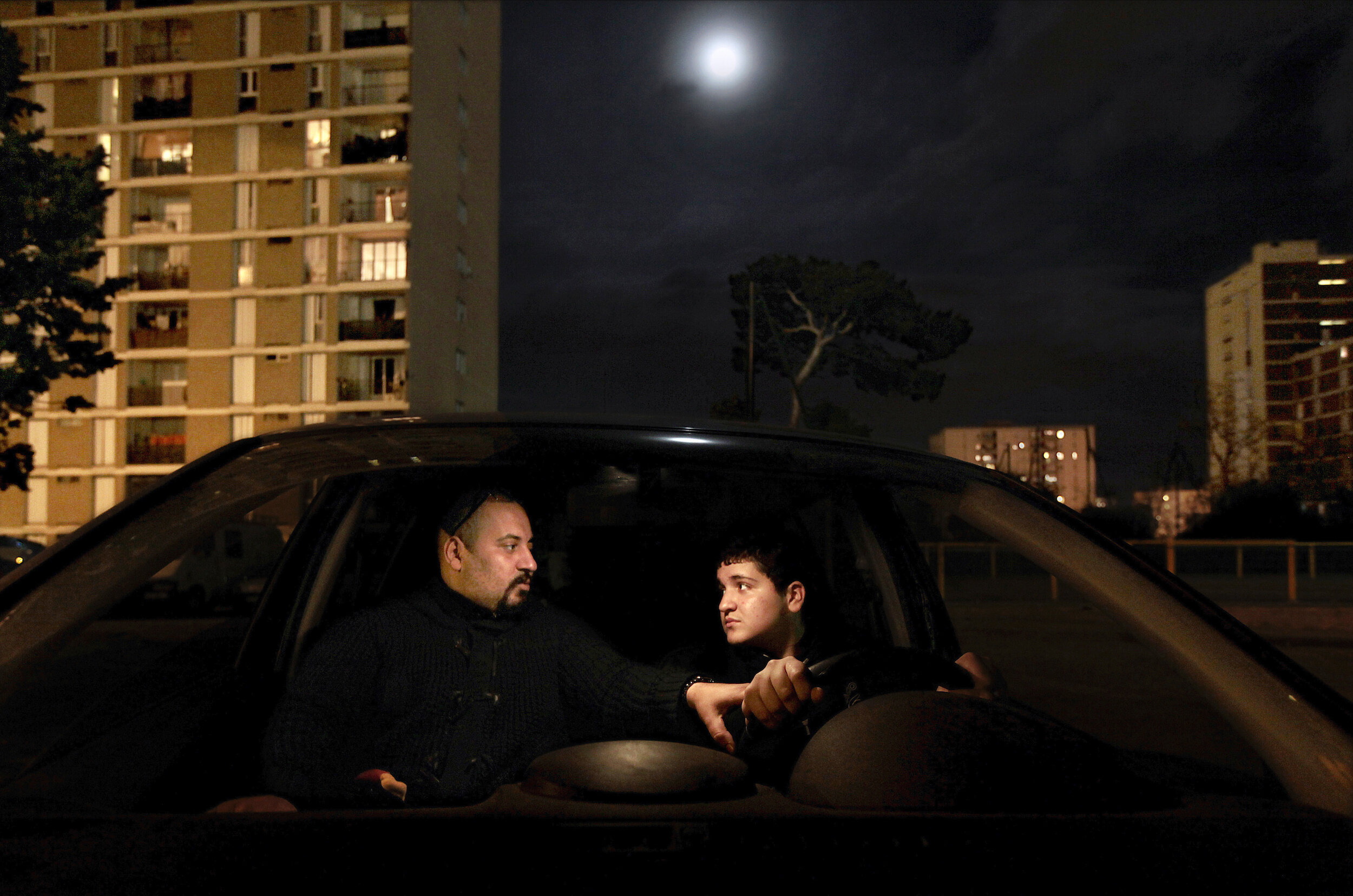     France. Marseille. 2012. Abdel Benfrih [right] was trying to convince his uncle to let him drive the car but his uncle refused, as Abdel is a minor without a driving license. Abdel and his family lives in a cité – social housing project – in the 