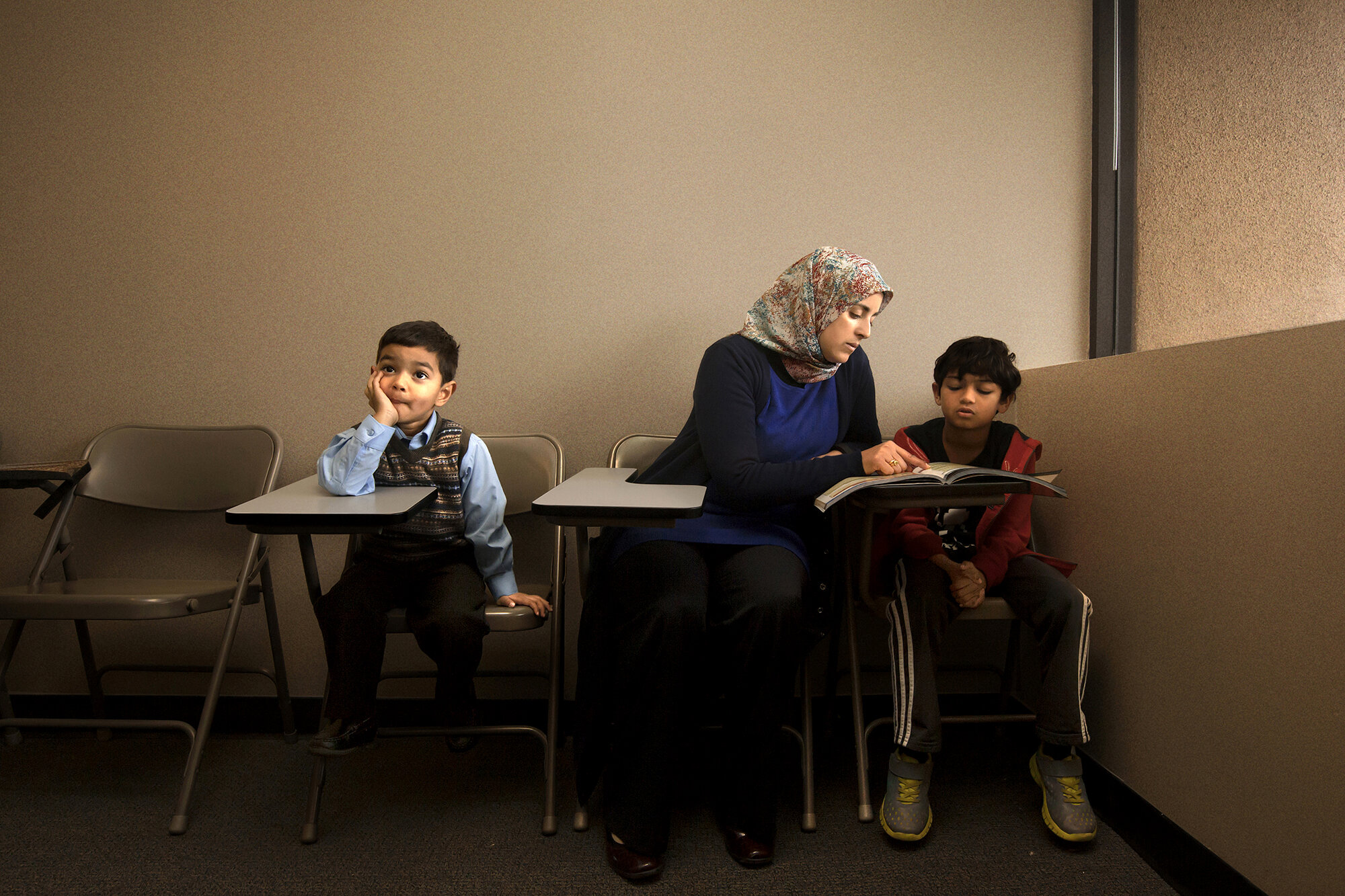   USA. Pleasanton, California. 2018. A teacher (center) with a student during a Sunday Quran class while her son (left) waits for her.  
