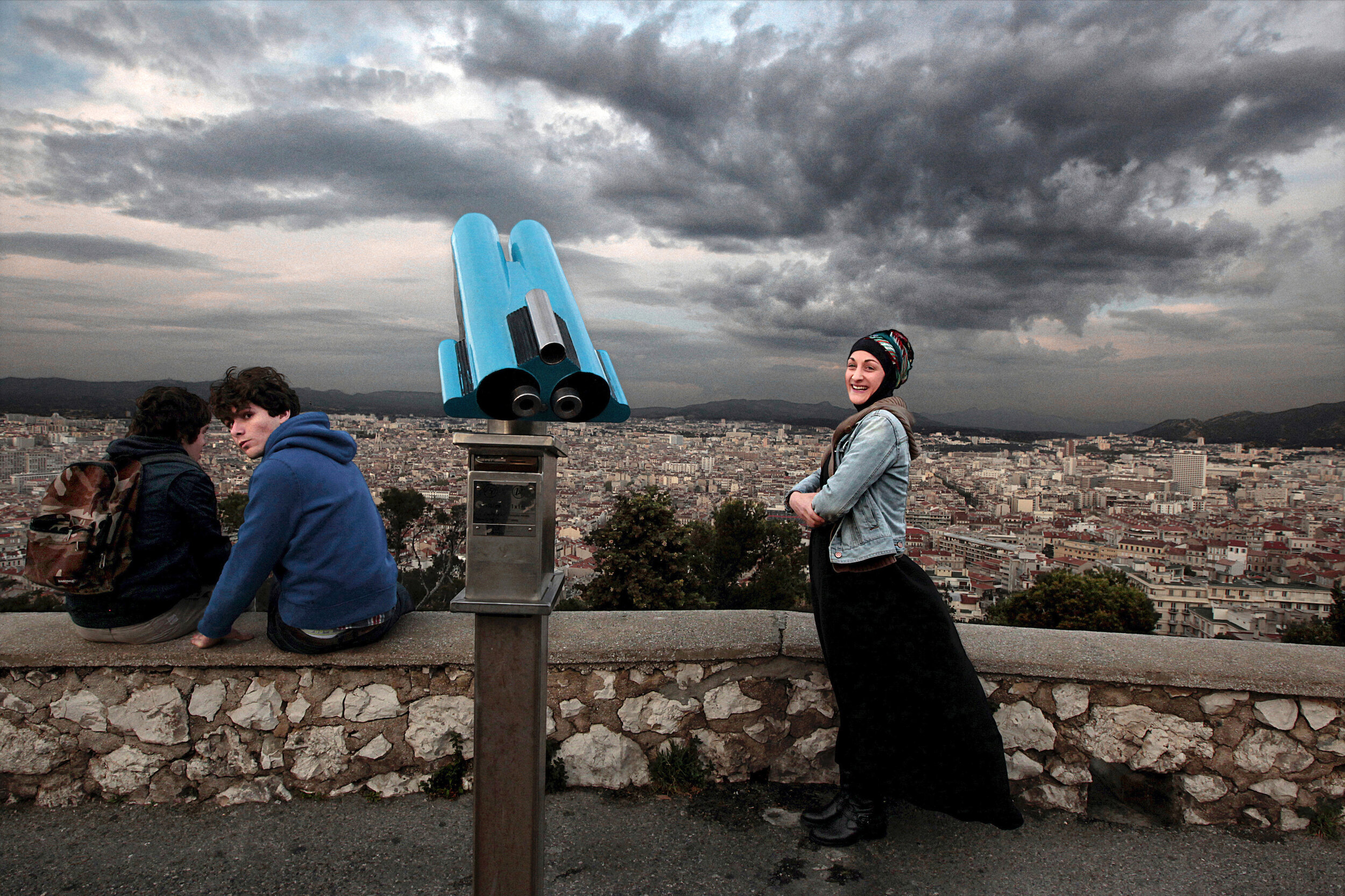   France. Marseille. 2014. Camille (right), a convert to Islam, enjoys the view atop the hill of Notre Dame de la Garde. On being asked why she embraced Islam, she said, “A few years ago, while walking I saw many Muslim men praying on the side of a b