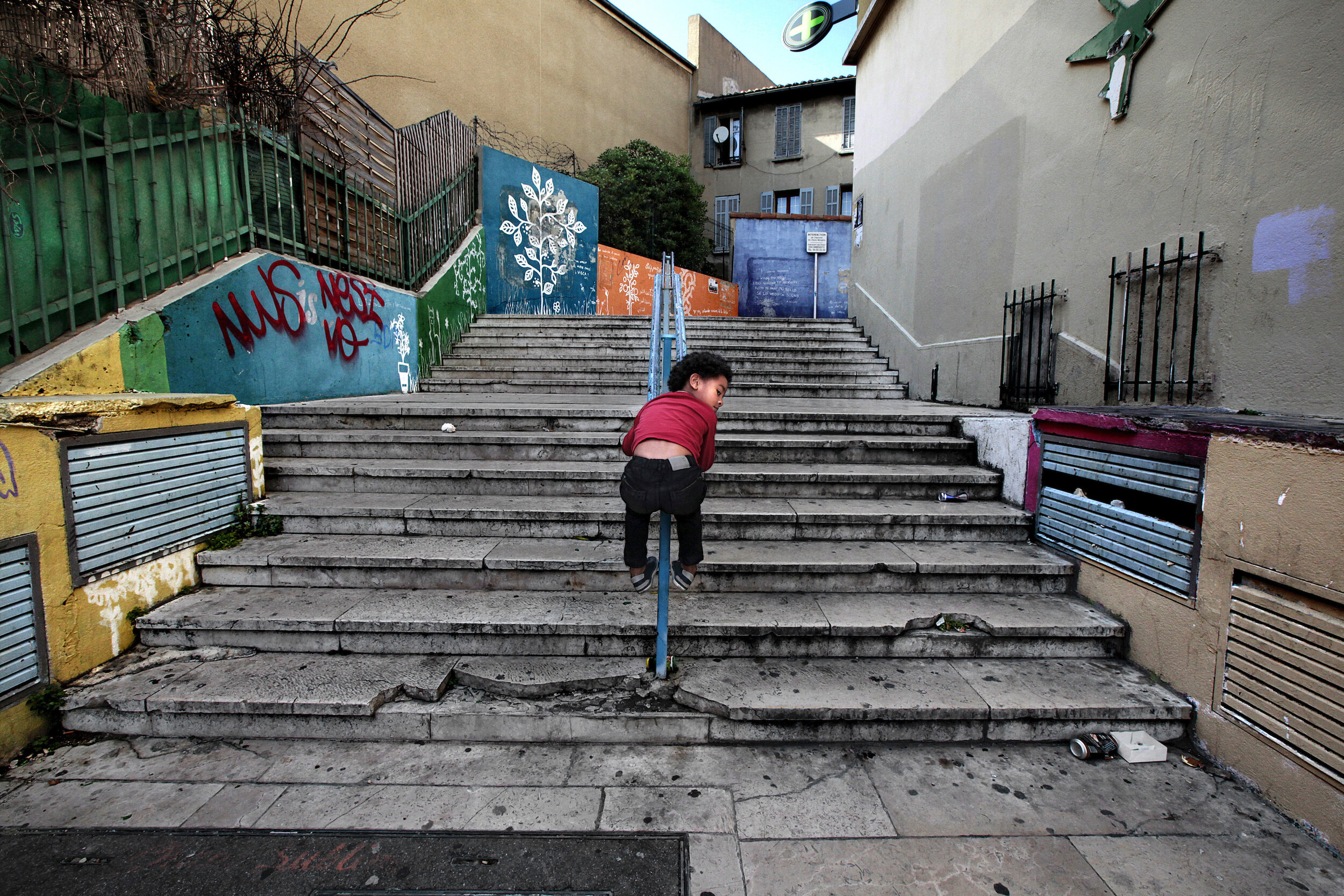   France. Marseille. 2014. A child slides down the stairs at a street in the 3rd arrondissement. Home to a very large and diverse immigrant population, the 3rd arrondissement is known for its deprivation and increasing poverty in comparison with othe