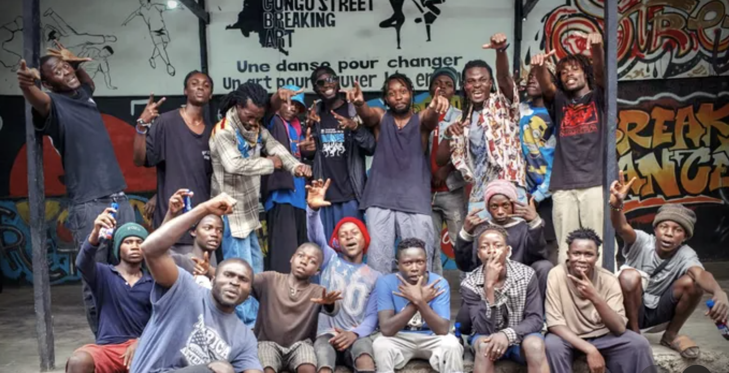 Group of young people posing together in front of colorful graffiti art, some making hand gestures and others smiling.
