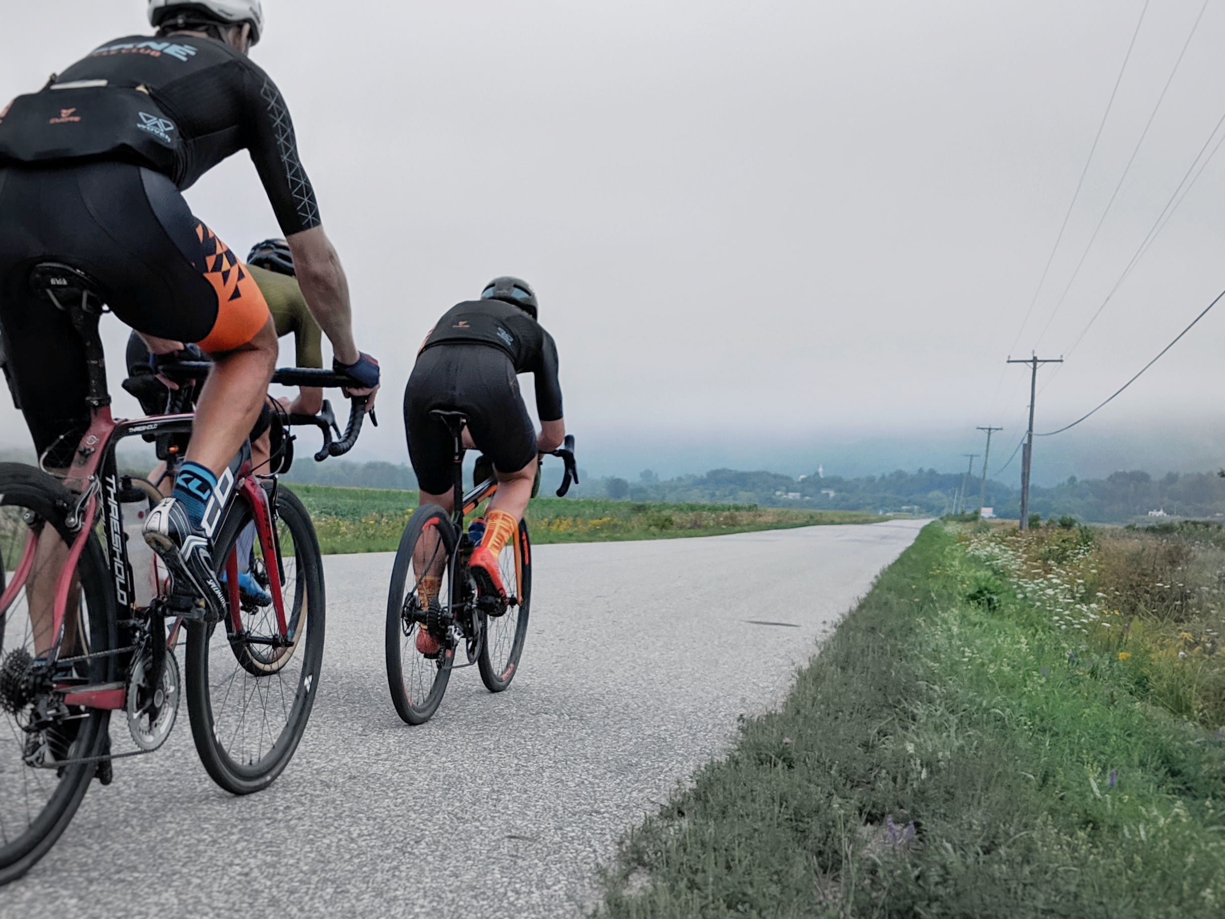 A group of cyclists riding on a rural country road on a cloudy day.