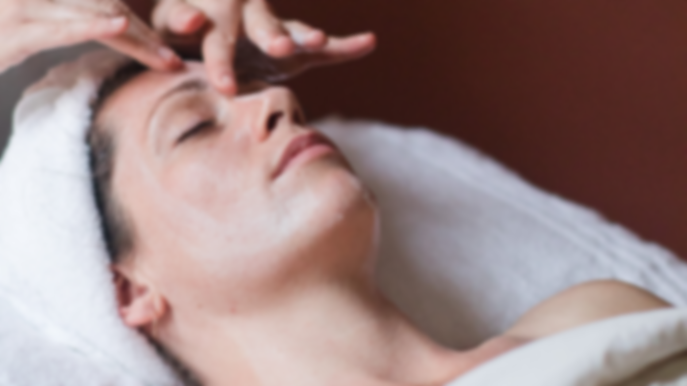 Person receiving a facial massage while lying on a treatment table with eyes closed