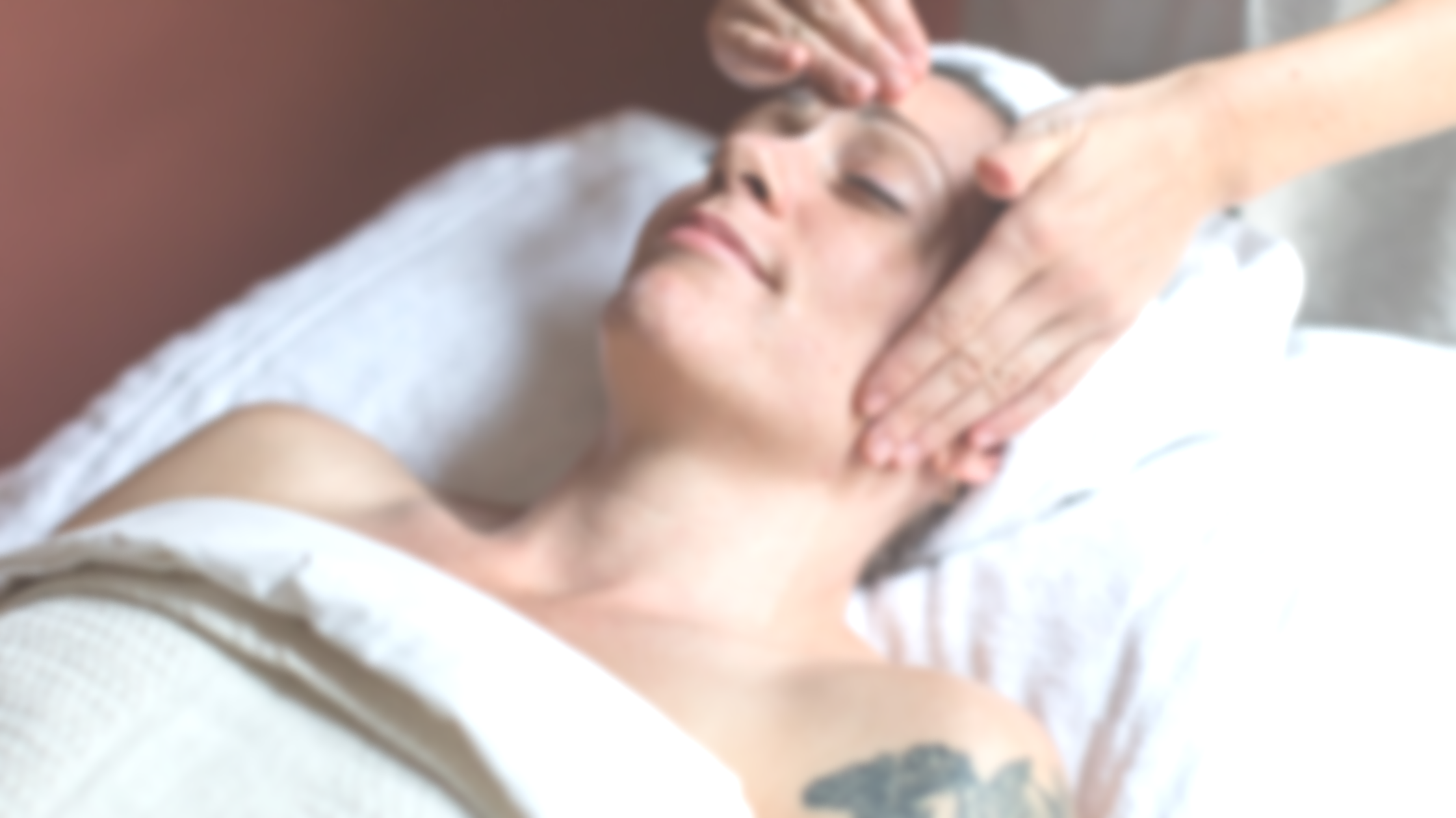 A woman receiving a facial massage while lying on a massage table, with eyes closed and a relaxed expression.