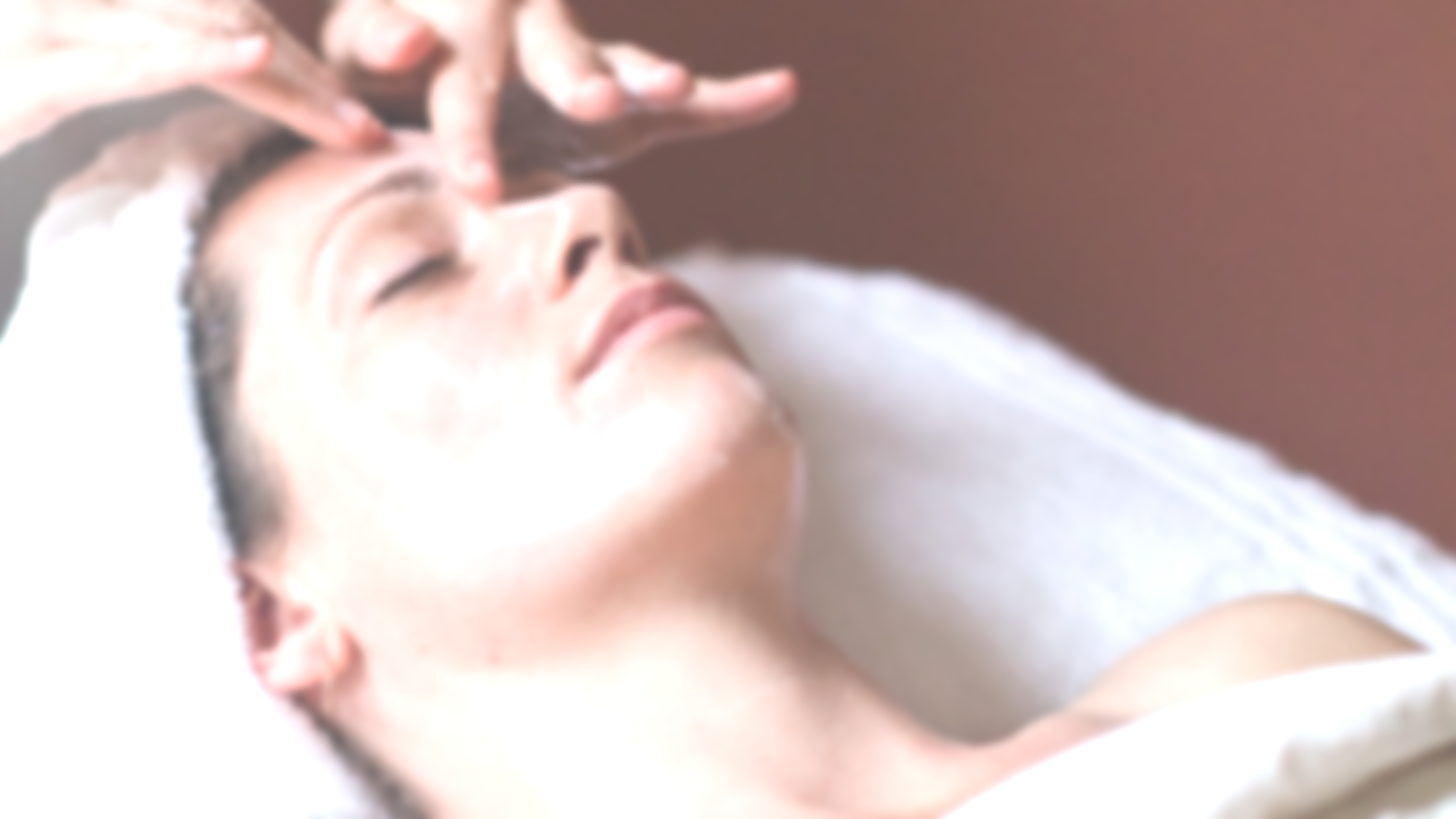 Person receiving a facial massage while lying on a treatment table with eyes closed