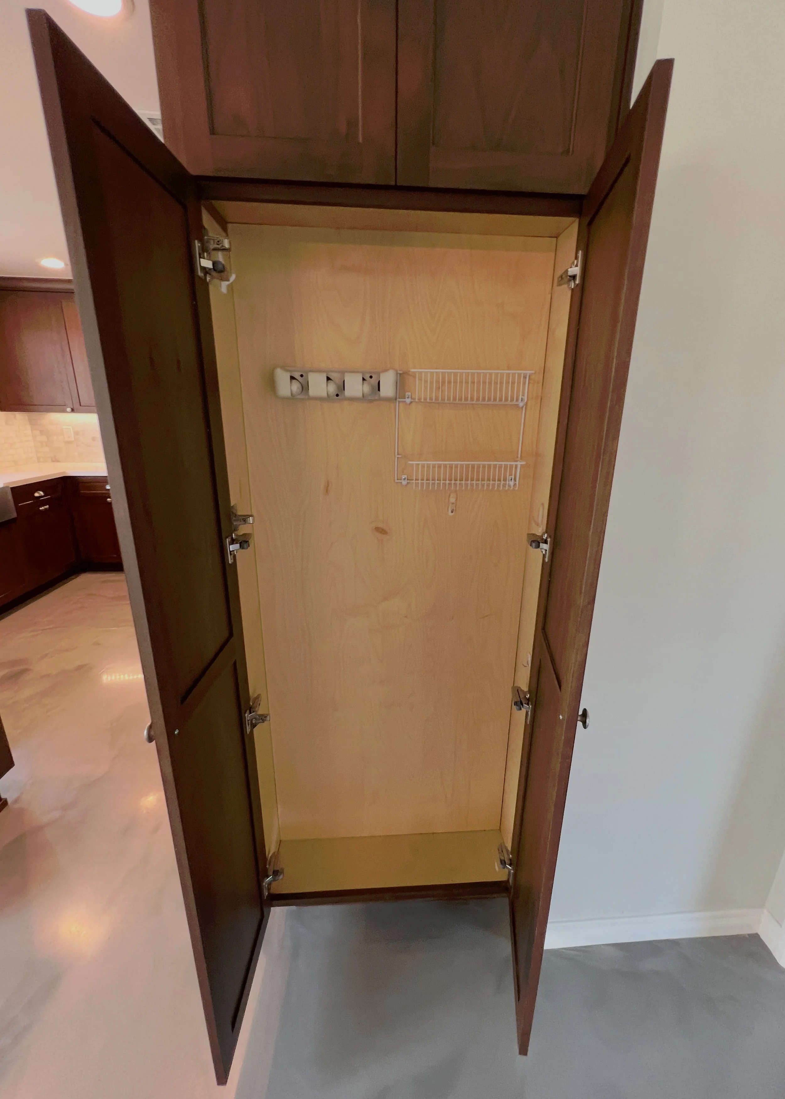Empty kitchen cabinet with mounted wire rack and electrical outlet inside.