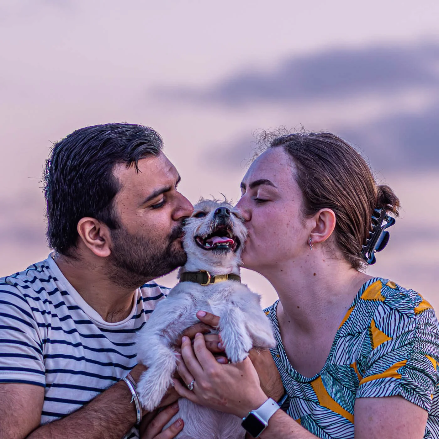 man and woman kissing their dog by the ocean