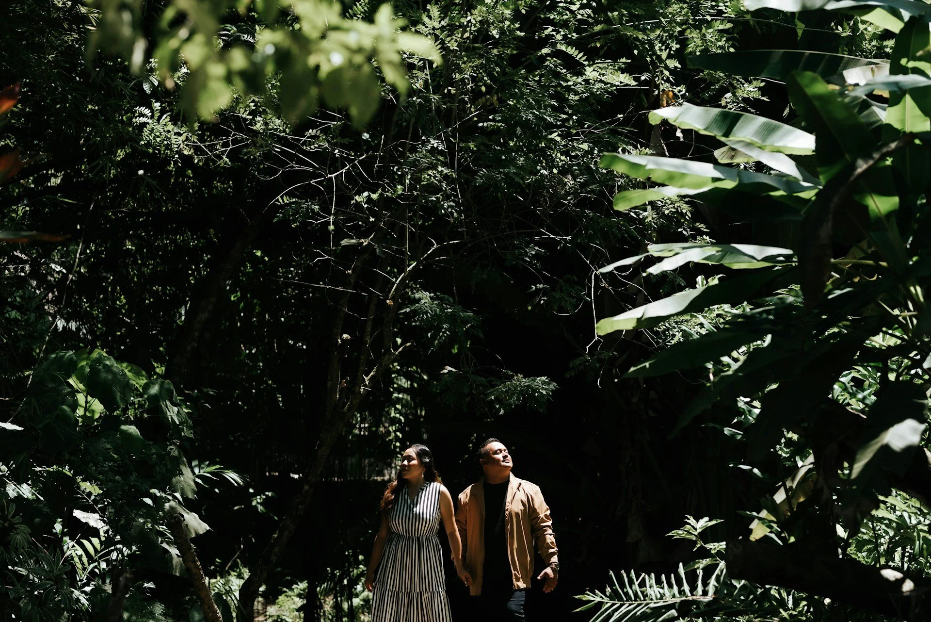 A man and a woman holding hands while walking through a lush, green jungle.
