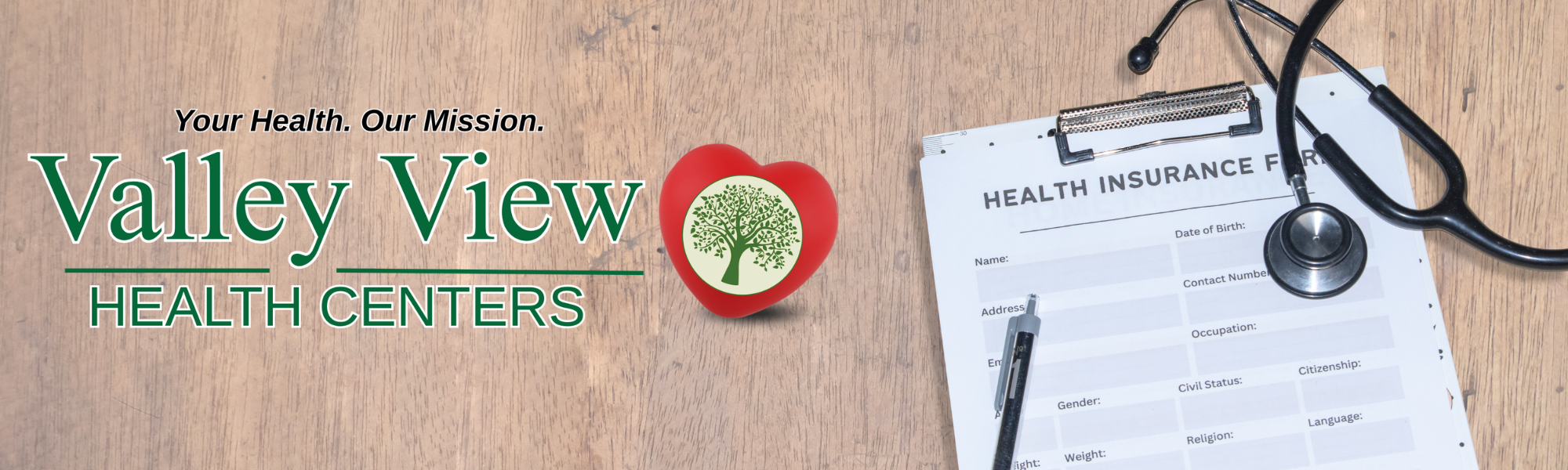 A wooden table with a stethoscope, a clipboard with a health insurance form, a pen, a red heart-shaped object with a green tree logo, and text that reads, 'Your Health. Our Mission. Valley View Health Centers.'