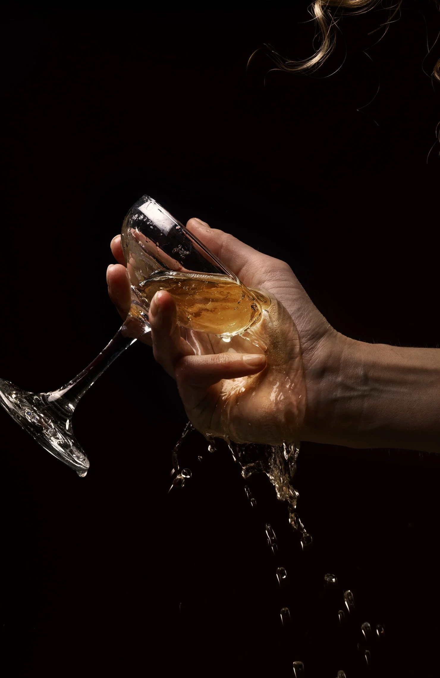 A hand holding a glass of spilled Barbet, with liquid dripping down.