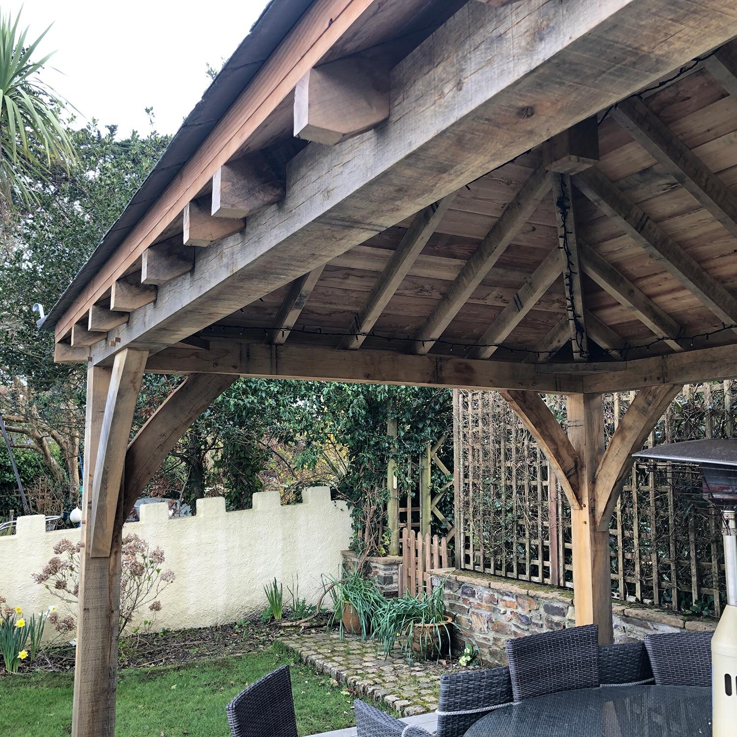 Green oak trusses and rafters providing shelter for garden dining space